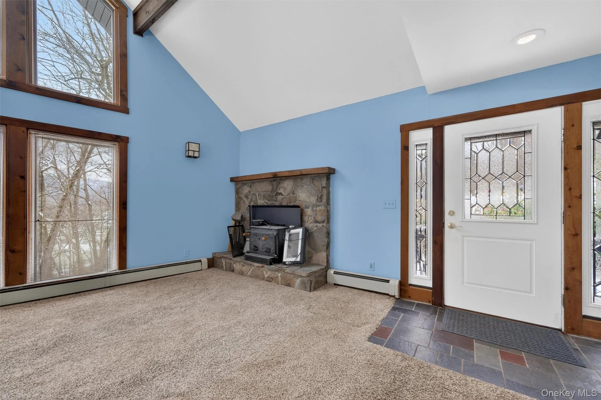 Foyer featuring healthy amount of natural light, a wood stove, baseboard heating, high vaulted ceiling, and beamed ceiling Foyer featuring healthy amount of natural light, a wood stove, baseboard heating, high vaulted ceiling, and beamed ceiling