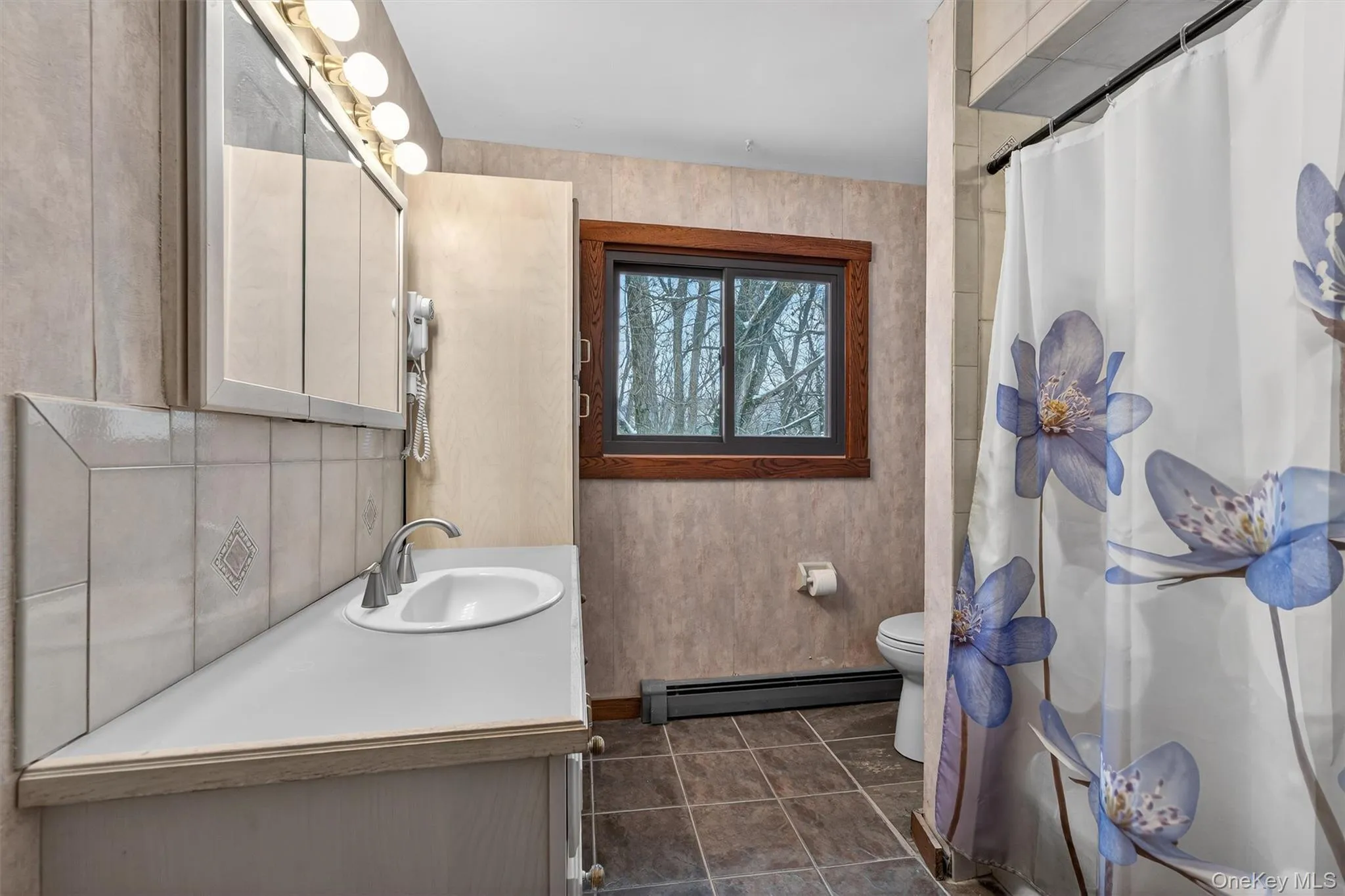 Full bath with curtained shower, vanity, baseboard heating, and dark tile patterned floors Full bath with curtained shower, vanity, baseboard heating, and dark tile patterned floors
