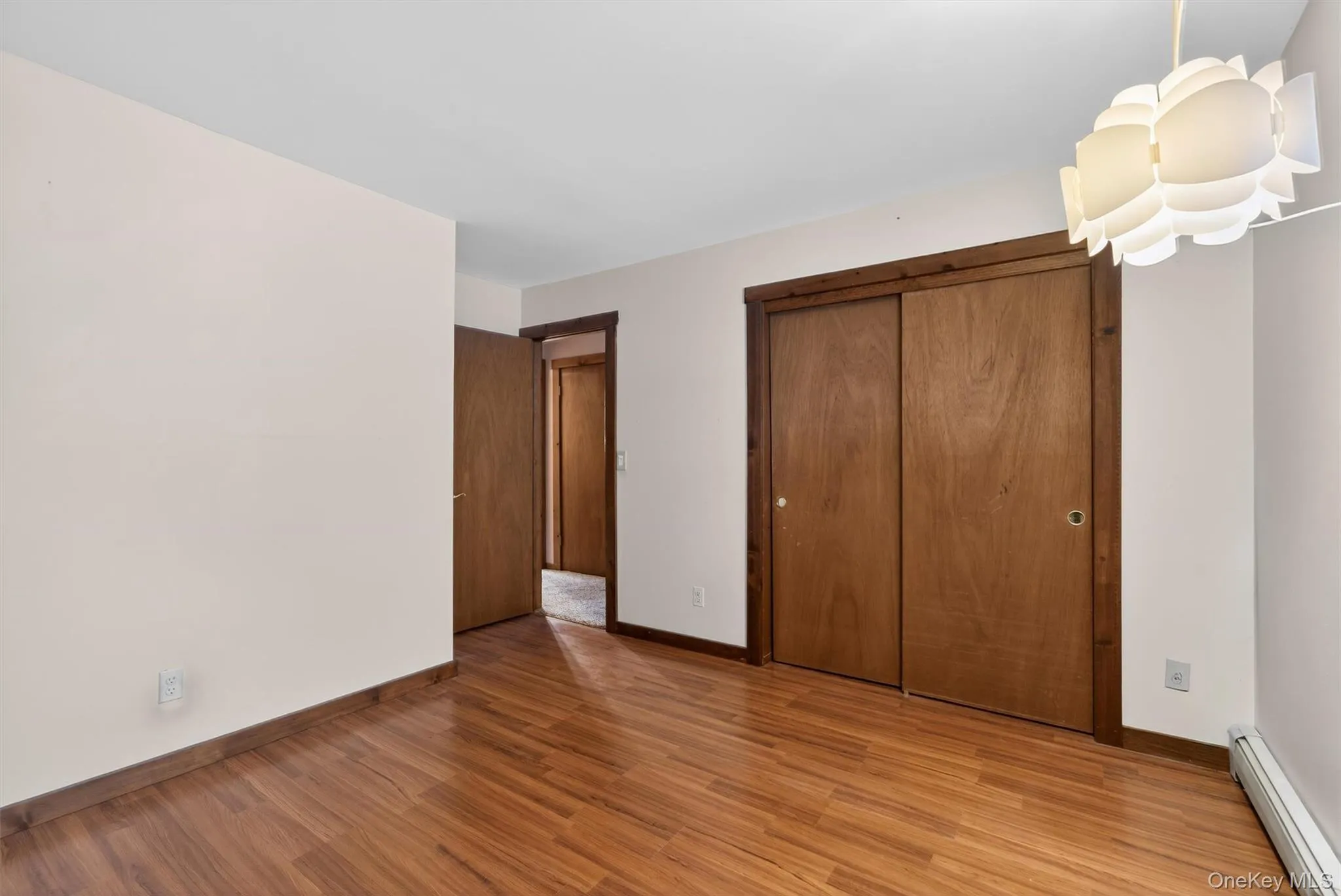 Unfurnished bedroom featuring a baseboard heating unit, light wood-style floors, and a closet Unfurnished bedroom featuring a baseboard heating unit, light wood-style floors, and a closet