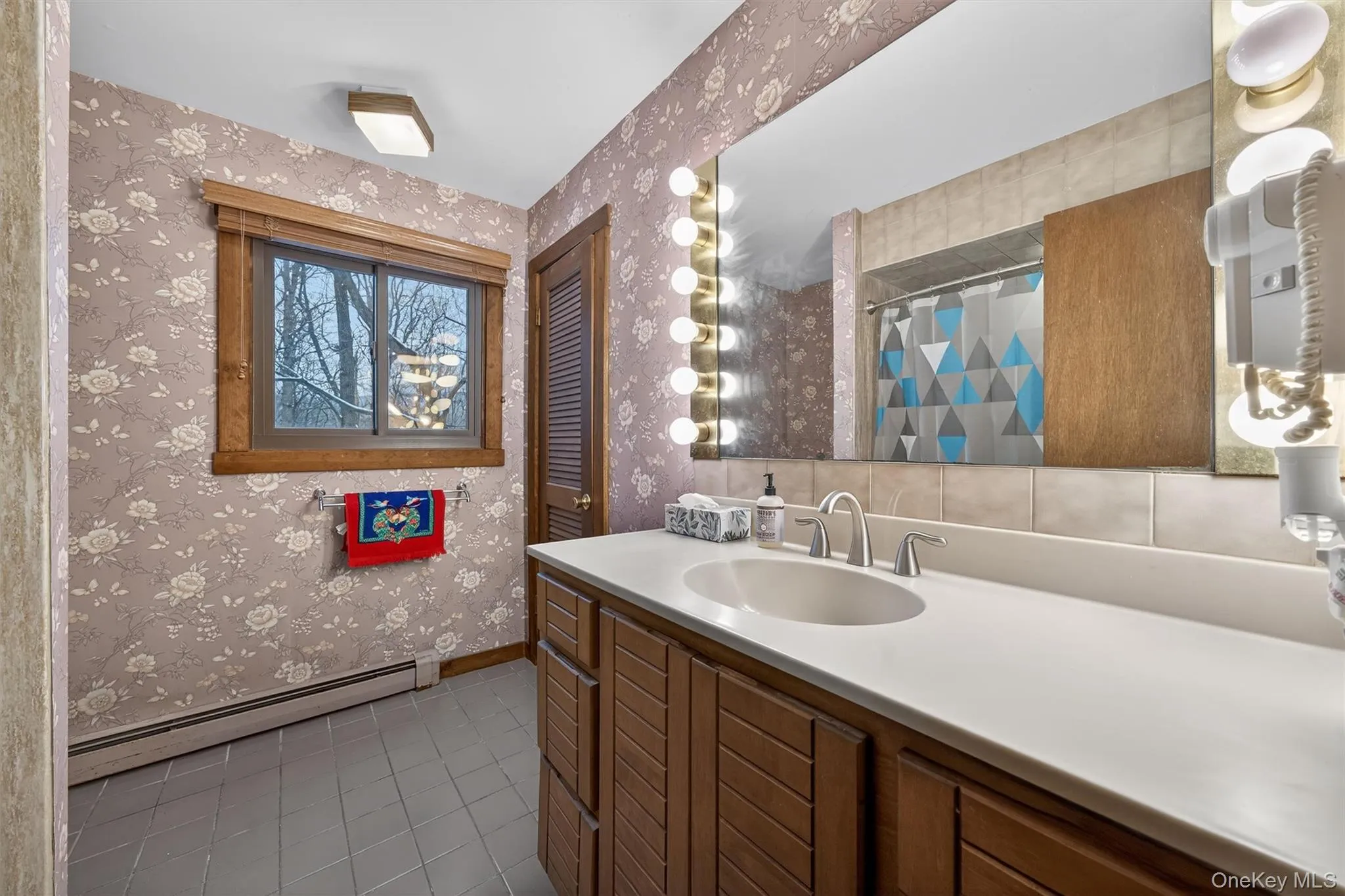 Bathroom with a baseboard heating unit, dark tile patterned floors, vanity, a shower with shower curtain, and wallpapered walls Bathroom with a baseboard heating unit, dark tile patterned floors, vanity, a shower with shower curtain, and wallpapered walls