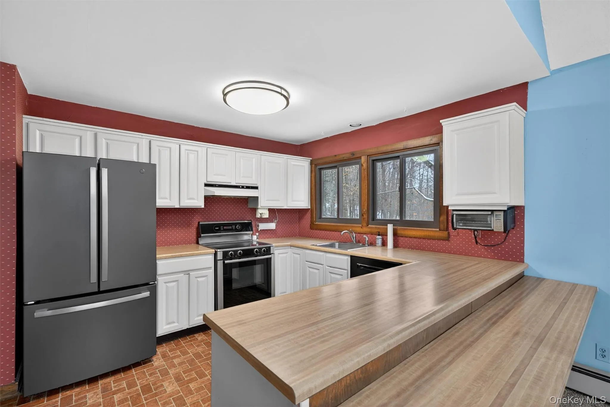 Kitchen with freestanding refrigerator, electric range oven, brick patterned floors, a peninsula, and light countertops Kitchen with freestanding refrigerator, electric range oven, brick patterned floors, a peninsula, and light countertops