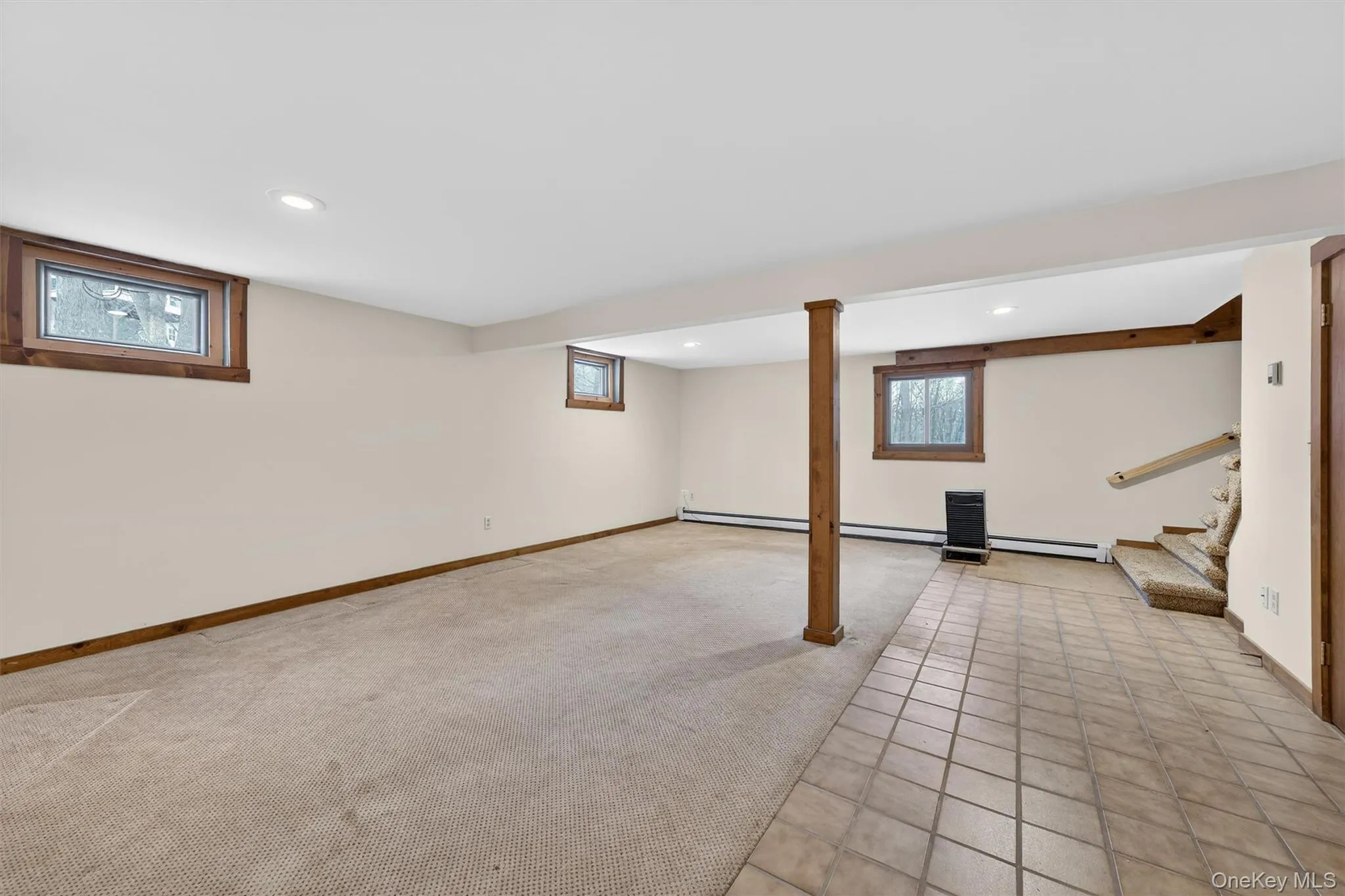 Below grade area with light carpet, stairway, recessed lighting, light tile patterned floors, and a baseboard radiator Below grade area with light carpet, stairway, recessed lighting, light tile patterned floors, and a baseboard radiator