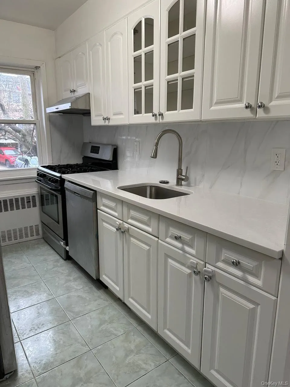 Kitchen with stainless steel appliances, white cabinets, glass insert cabinets, radiator, and light stone countertops Kitchen with stainless steel appliances, white cabinets, glass insert cabinets, radiator, and light stone countertops