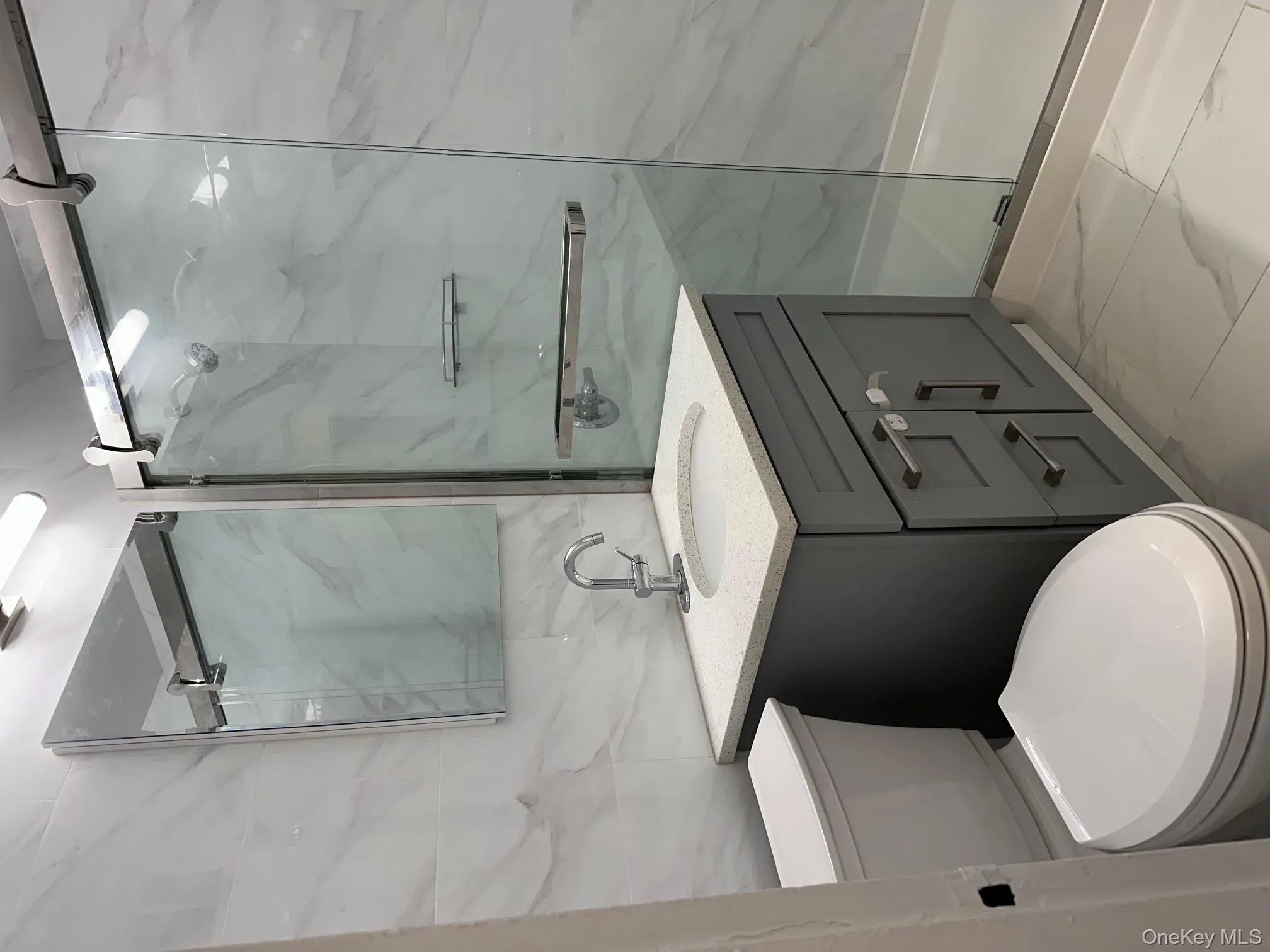 Full bathroom with vanity, tile walls, light marble finish floors, and a marble finish shower Full bathroom with vanity, tile walls, light marble finish floors, and a marble finish shower