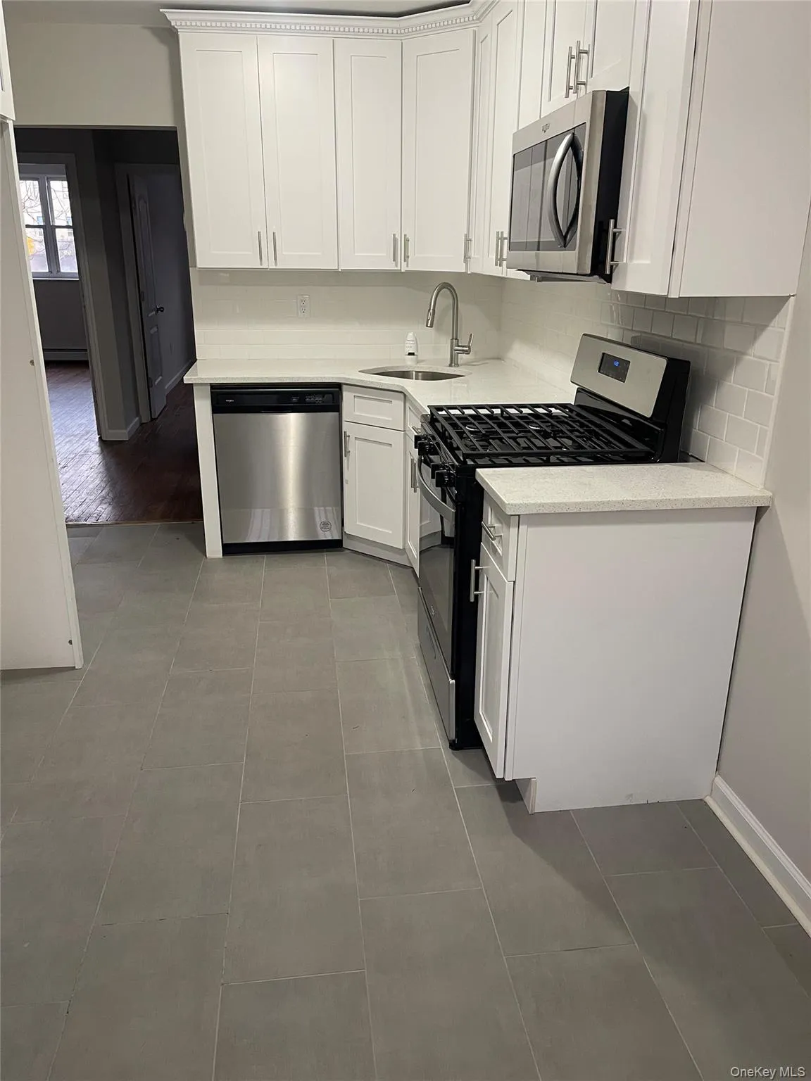 Kitchen with appliances with stainless steel finishes, white cabinetry, light stone countertops, backsplash, and light tile patterned flooring Kitchen with appliances with stainless steel finishes, white cabinetry, light stone countertops, backsplash, and light tile patterned flooring