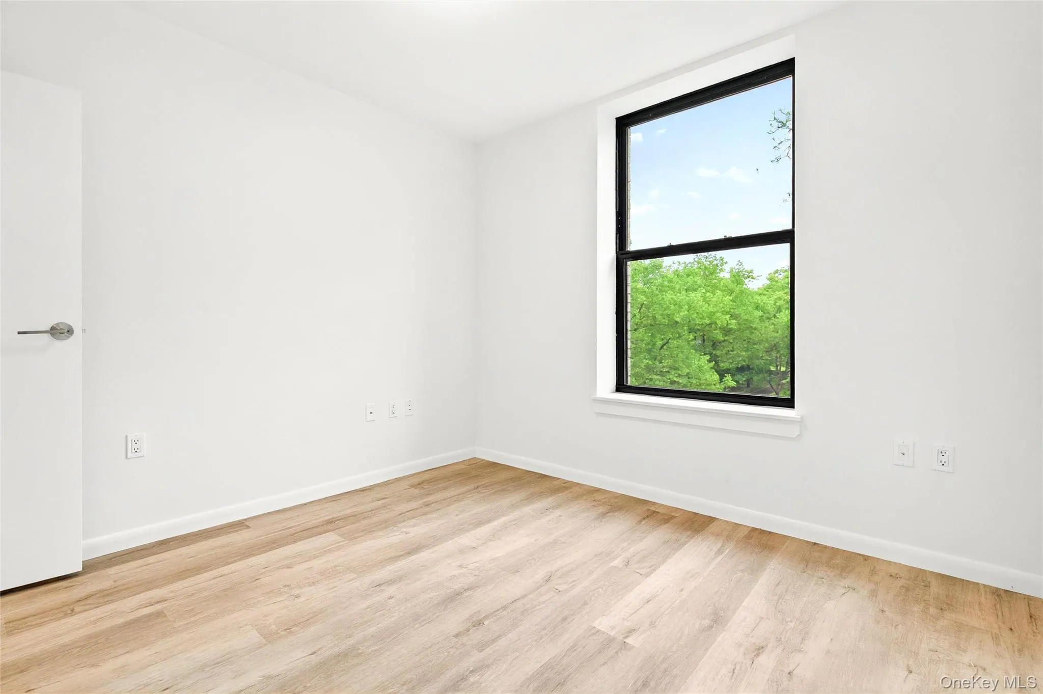 Bedroom with an AC wall unit, light wood finished floors, and baseboards Bedroom with an AC wall unit, light wood finished floors, and baseboards