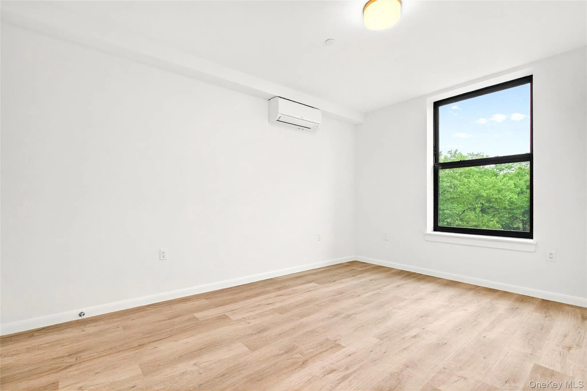 Bedroom with an AC wall unit, light wood finished floors, and baseboards Bedroom with an AC wall unit, light wood finished floors, and baseboards