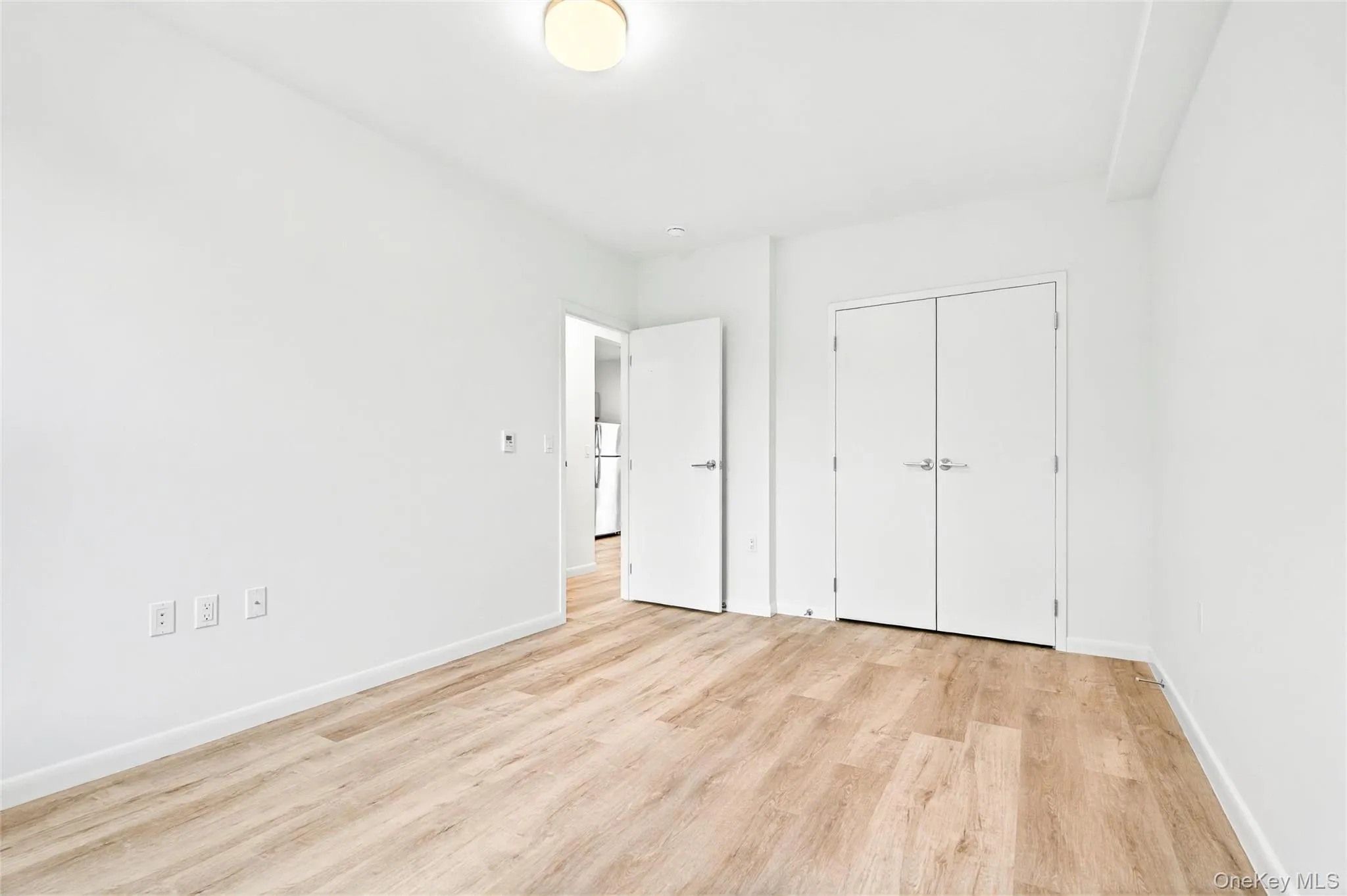 Bedroom with an AC wall unit, light wood finished floors, and baseboards Bedroom with an AC wall unit, light wood finished floors, and baseboards