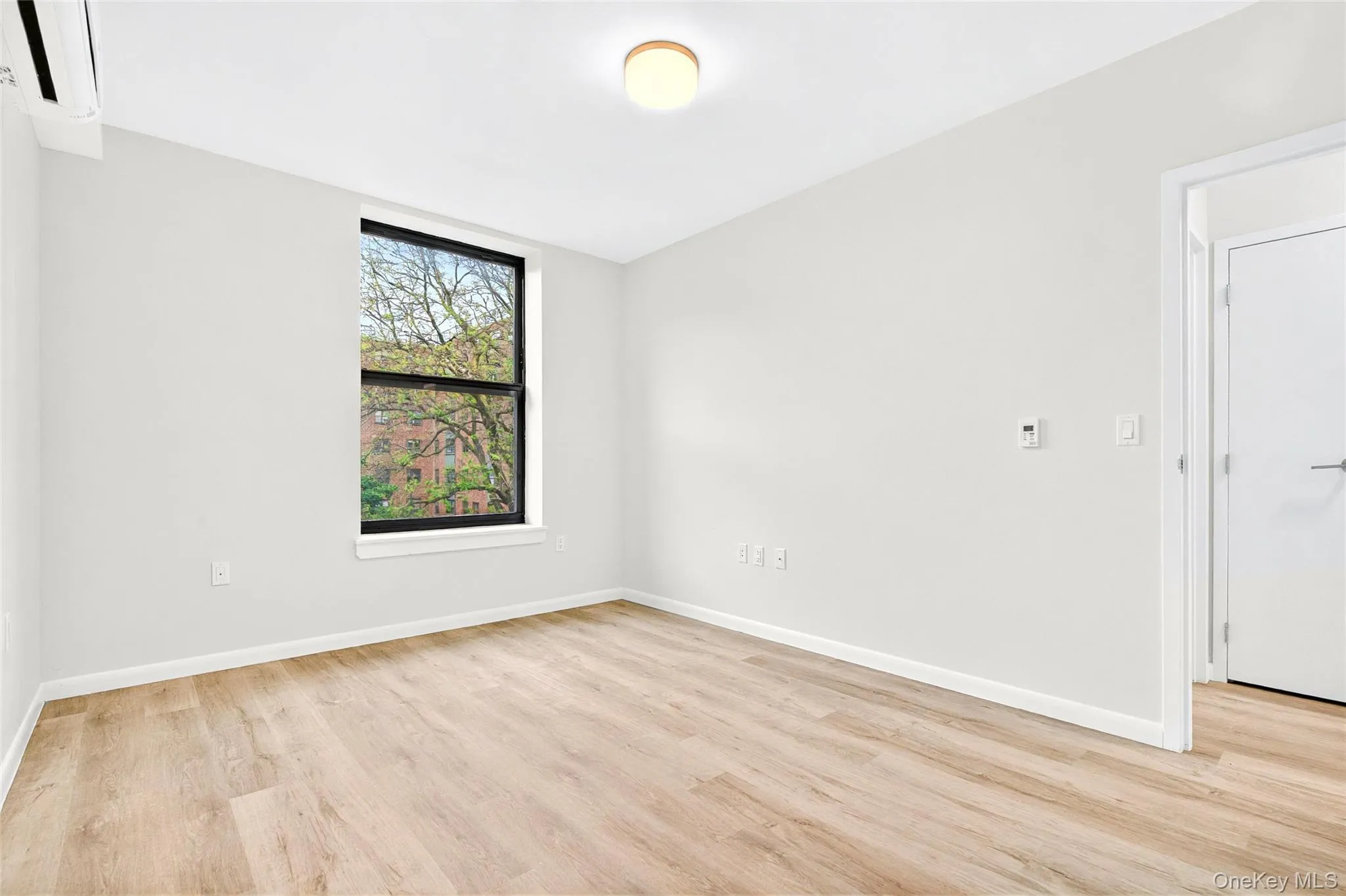 Bedroom with an AC wall unit, light wood finished floors, and baseboards Bedroom with an AC wall unit, light wood finished floors, and baseboards