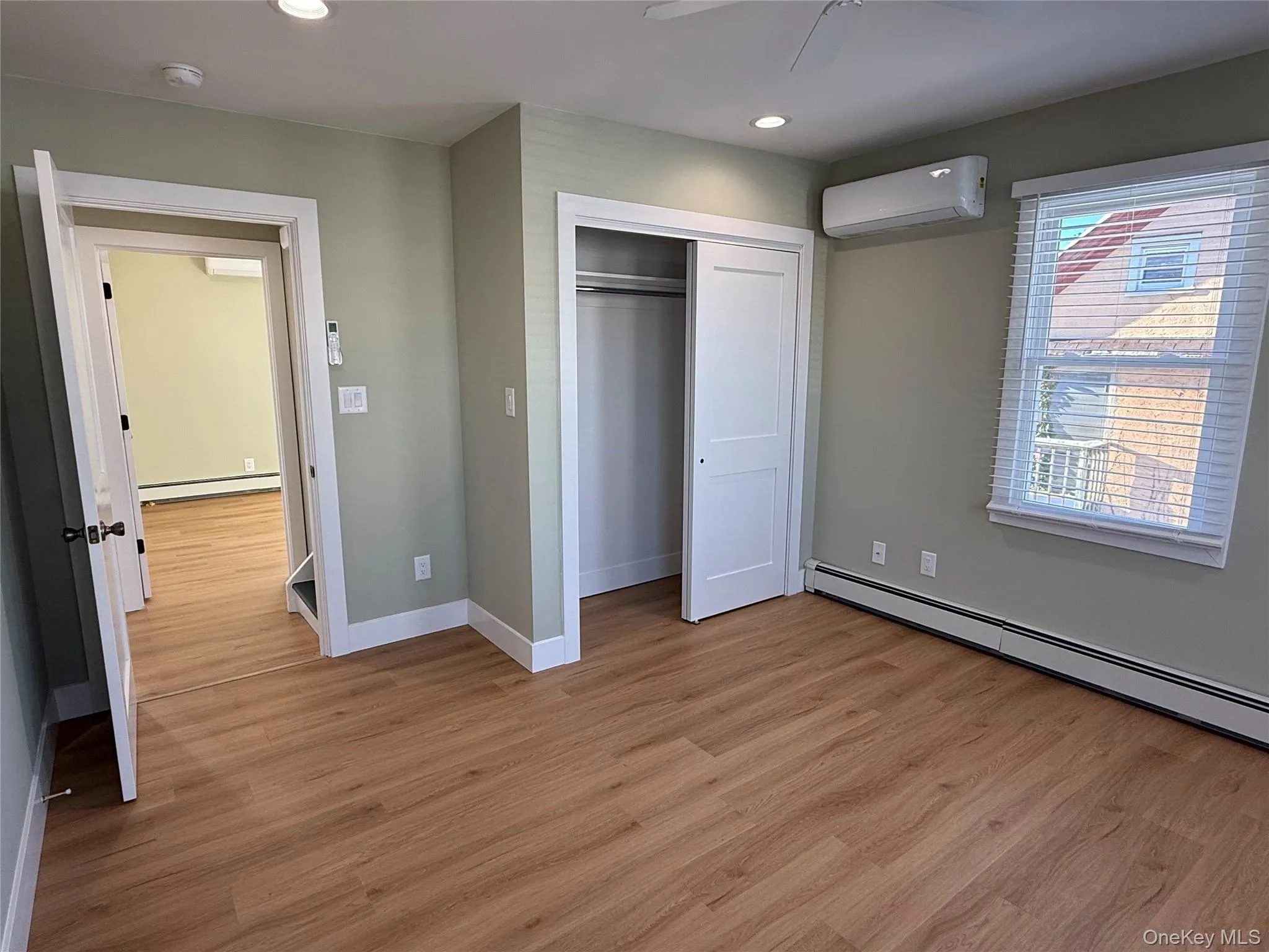 Unfurnished bedroom with light wood-style flooring, a wall unit AC, a closet, recessed lighting, and baseboard heating Unfurnished bedroom with light wood-style flooring, a wall unit AC, a closet, recessed lighting, and baseboard heating