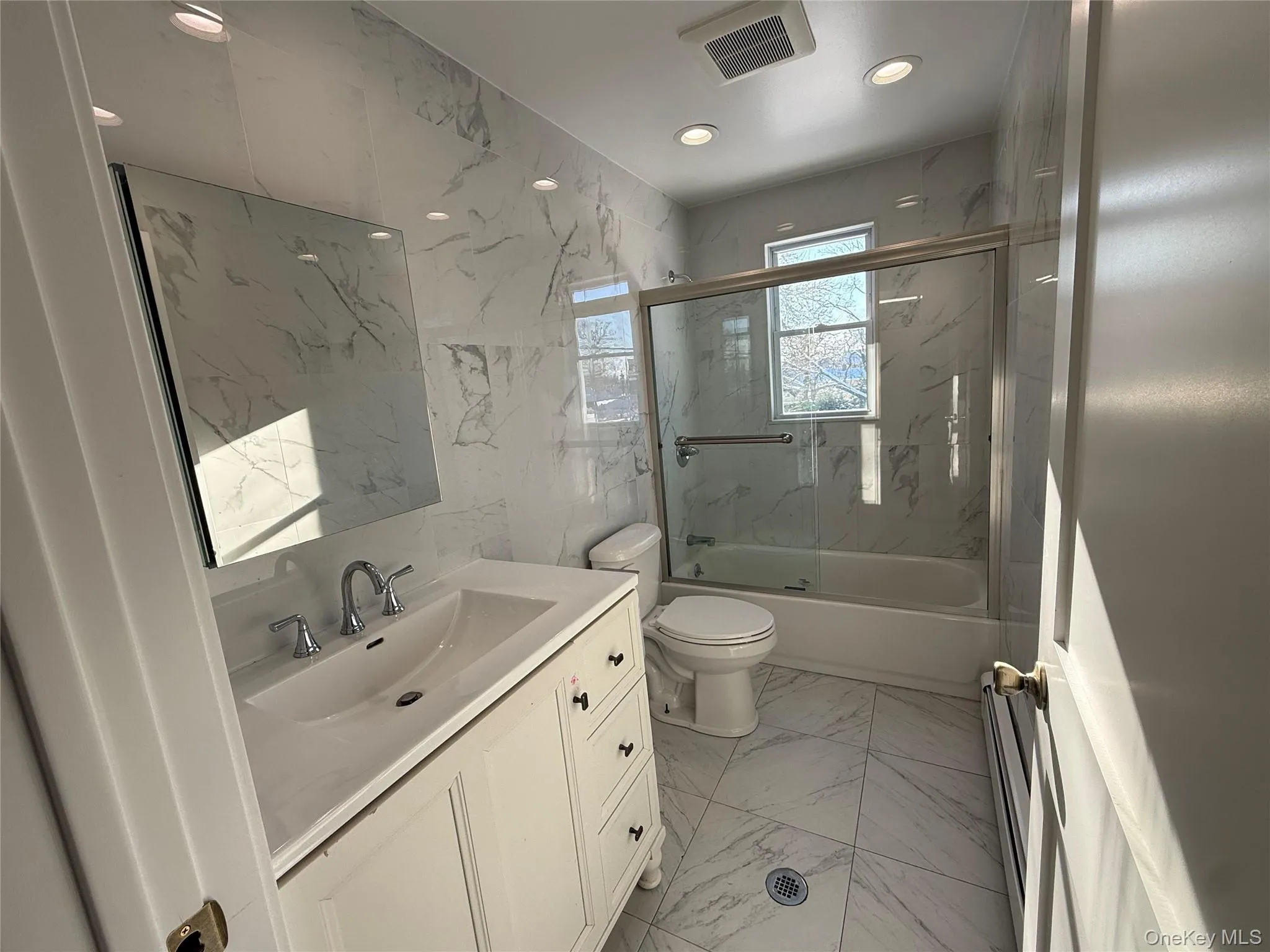 Full bathroom with light marble finish floors, vanity, bath / shower combo with glass door, tile walls, and stone wall Full bathroom with light marble finish floors, vanity, bath / shower combo with glass door, tile walls, and stone wall