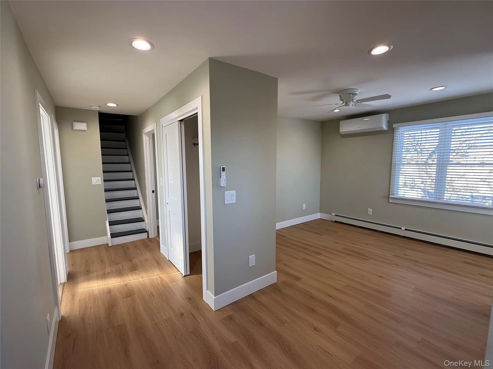 Hall featuring stairway, a baseboard heating unit, light wood-style flooring, recessed lighting, and an AC wall unit Hall featuring stairway, a baseboard heating unit, light wood-style flooring, recessed lighting, and an AC wall unit