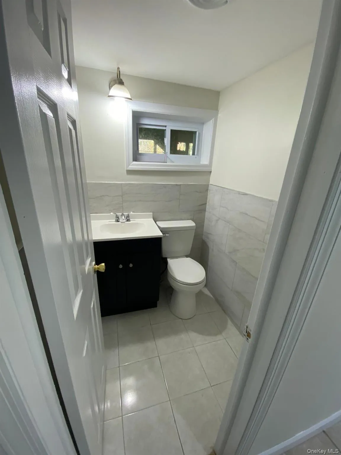 Bathroom with light tile patterned flooring, tile walls, vanity, and a wainscoted wall Bathroom with light tile patterned flooring, tile walls, vanity, and a wainscoted wall