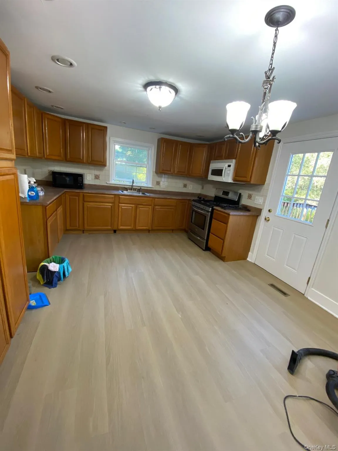 Kitchen featuring brown cabinetry, stainless steel range with gas cooktop, a chandelier, and hanging light fixtures Kitchen featuring brown cabinetry, stainless steel range with gas cooktop, a chandelier, and hanging light fixtures
