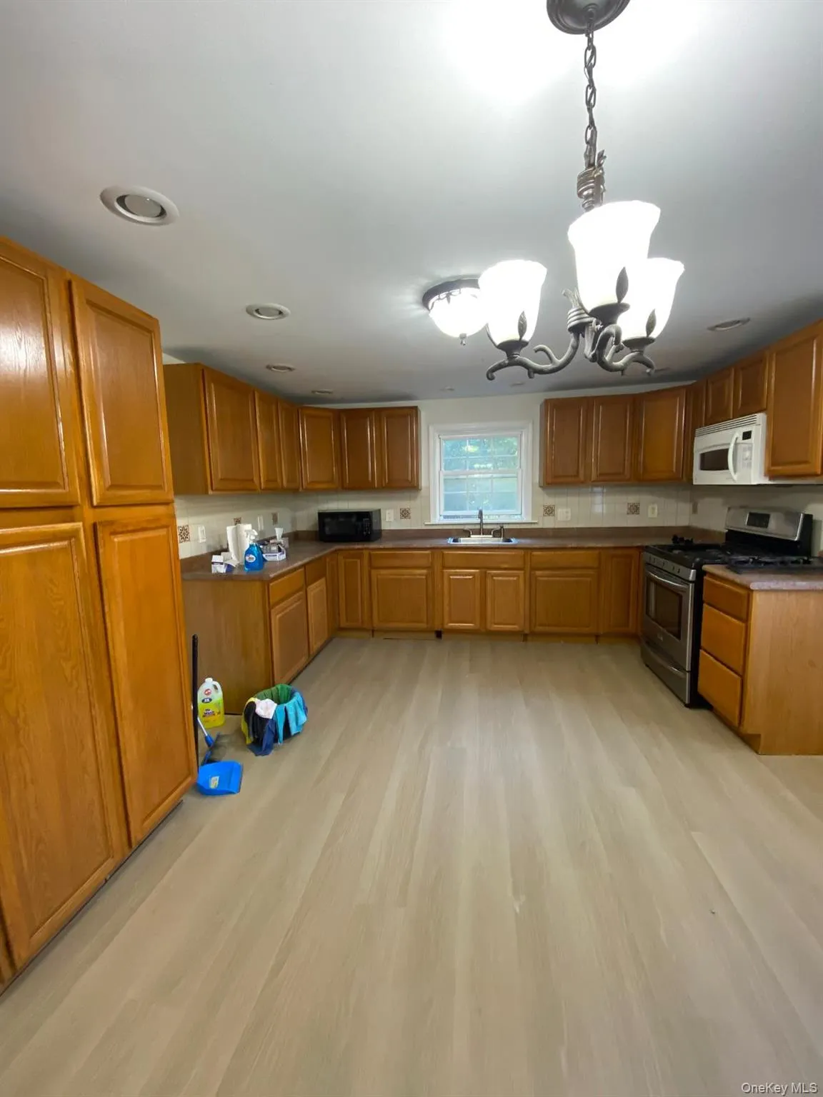 Kitchen with stainless steel gas range oven, a chandelier, brown cabinetry, and pendant lighting Kitchen with stainless steel gas range oven, a chandelier, brown cabinetry, and pendant lighting