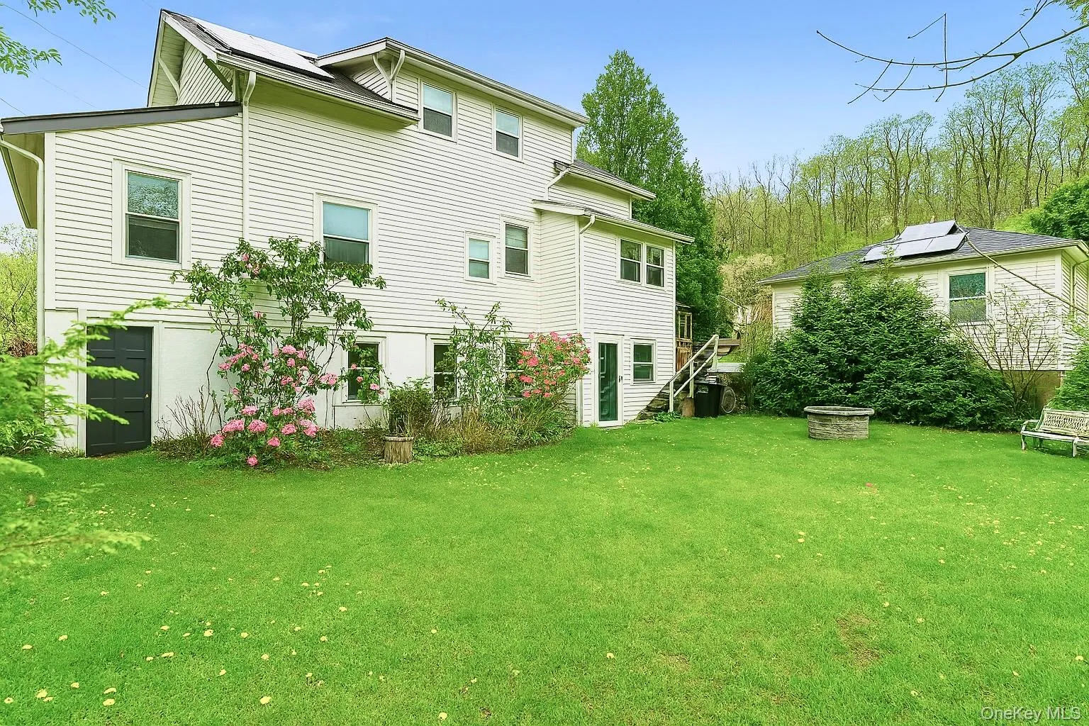 Rear view of the house in the summer with a level yard, and a fire pit Rear view of the house in the summer with a level yard, and a fire pit