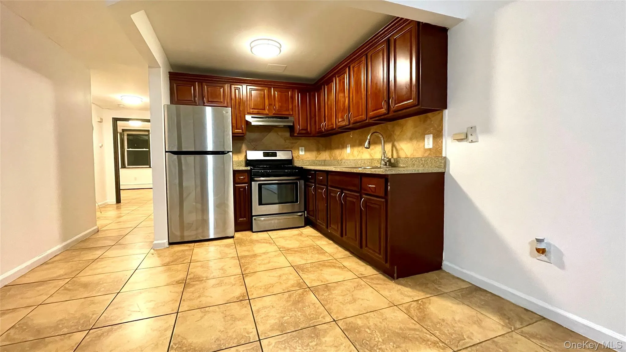 Kitchen with appliances with stainless steel finishes, decorative backsplash, under cabinet range hood, light tile patterned floors, and light stone counters Kitchen with appliances with stainless steel finishes, decorative backsplash, under cabinet range hood, light tile patterned floors, and light stone counters