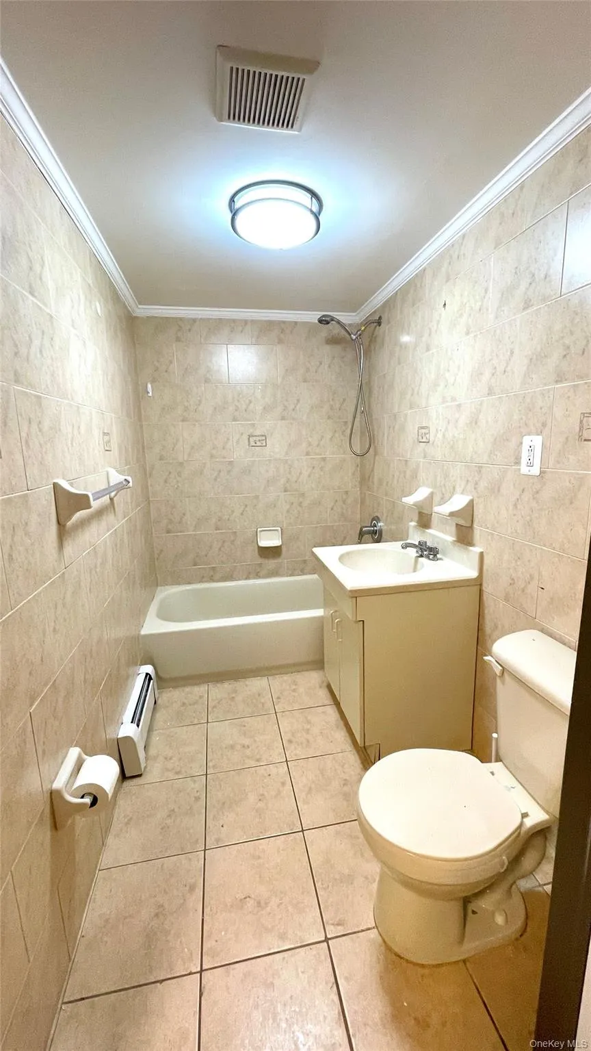 Bathroom with tile walls, vanity, light tile patterned floors, crown molding, and baseboard heating Bathroom with tile walls, vanity, light tile patterned floors, crown molding, and baseboard heating