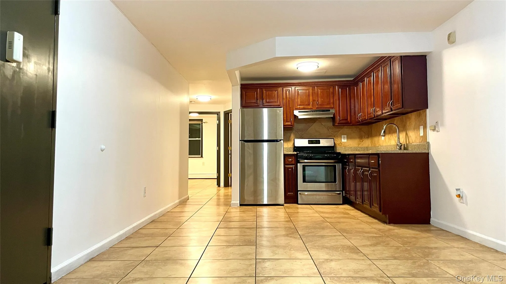 Kitchen with appliances with stainless steel finishes, light tile patterned floors, backsplash, under cabinet range hood, and light stone countertops Kitchen with appliances with stainless steel finishes, light tile patterned floors, backsplash, under cabinet range hood, and light stone countertops