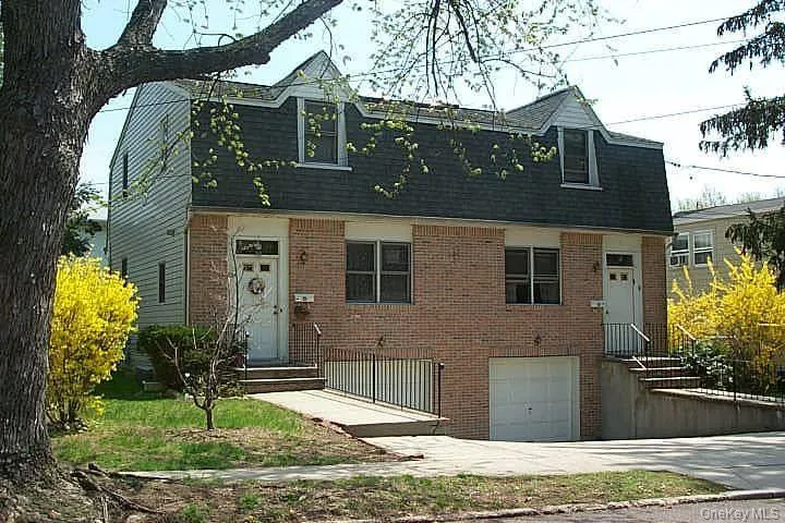 Dutch colonial with an attached garage, roof with shingles, brick siding, and driveway Dutch colonial with an attached garage, roof with shingles, brick siding, and driveway