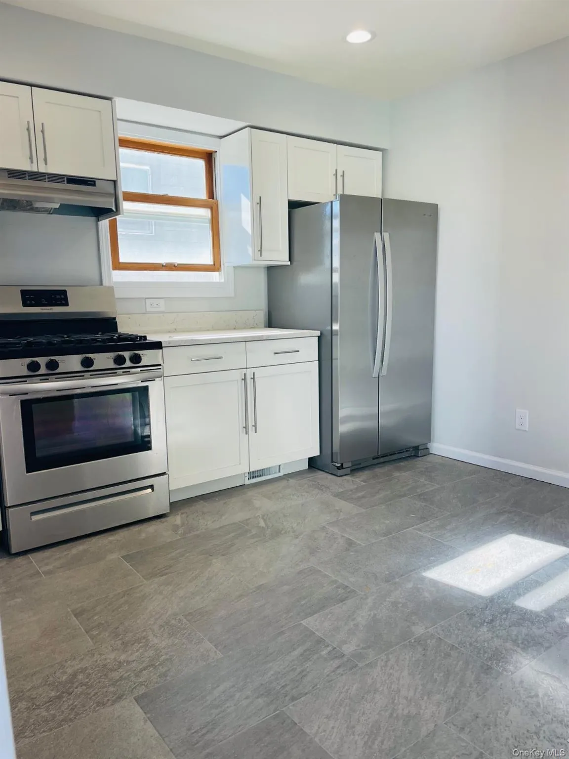 Kitchen featuring appliances with stainless steel finishes, under cabinet range hood, white cabinets, and light countertops Kitchen featuring appliances with stainless steel finishes, under cabinet range hood, white cabinets, and light countertops