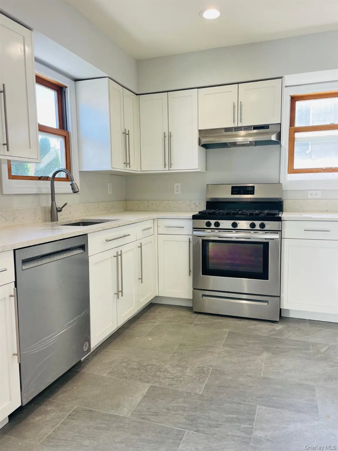 Kitchen with healthy amount of natural light, stainless steel appliances, white cabinetry, light stone countertops, and recessed lighting Kitchen with healthy amount of natural light, stainless steel appliances, white cabinetry, light stone countertops, and recessed lighting