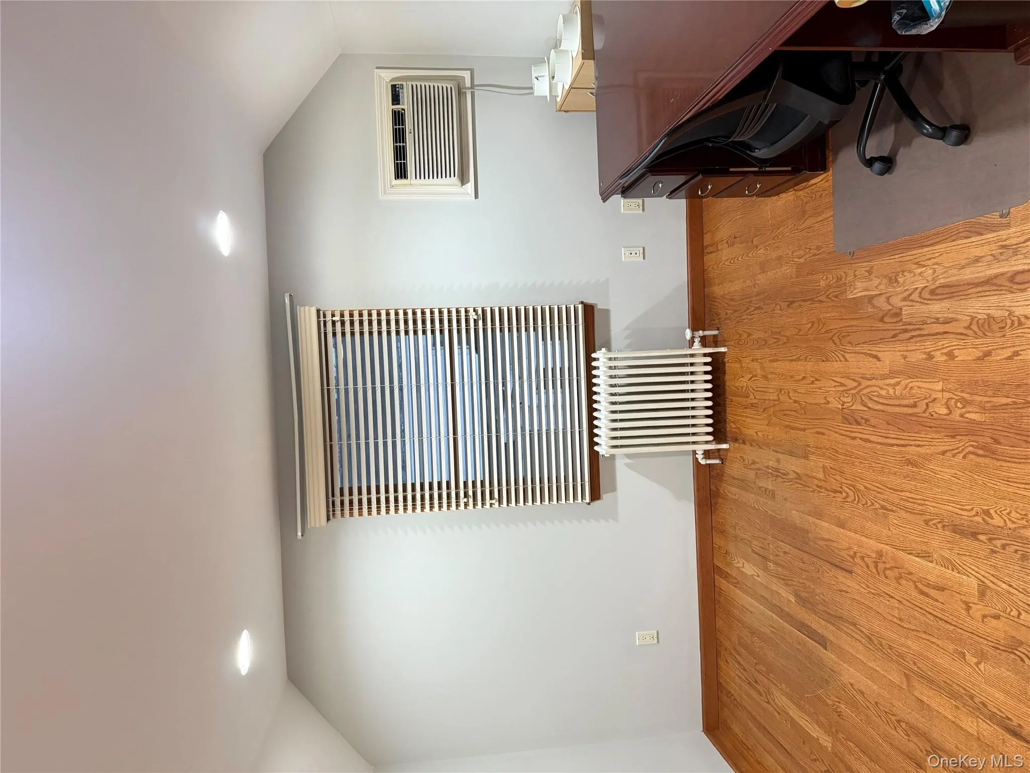 Office with radiator heating unit, lofted ceiling, light wood-style flooring, a wall unit AC, and recessed lighting Office with radiator heating unit, lofted ceiling, light wood-style flooring, a wall unit AC, and recessed lighting