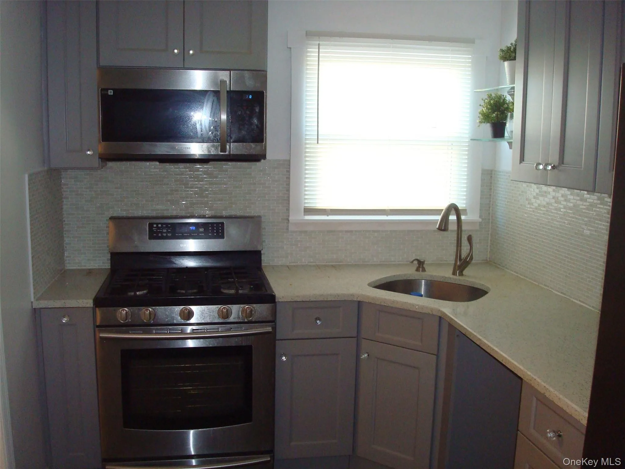 Kitchen featuring appliances with stainless steel finishes, light stone countertops, gray cabinets, and backsplash Kitchen featuring appliances with stainless steel finishes, light stone countertops, gray cabinets, and backsplash