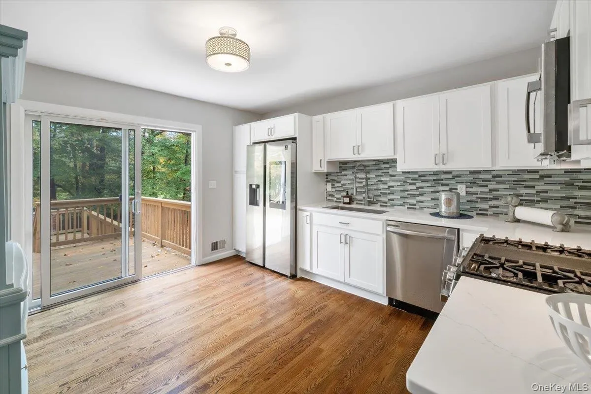 Kitchen with appliances with stainless steel finishes, light wood-type flooring, white cabinets, light stone countertops, and tasteful backsplash Kitchen with appliances with stainless steel finishes, light wood-type flooring, white cabinets, light stone countertops, and tasteful backsplash