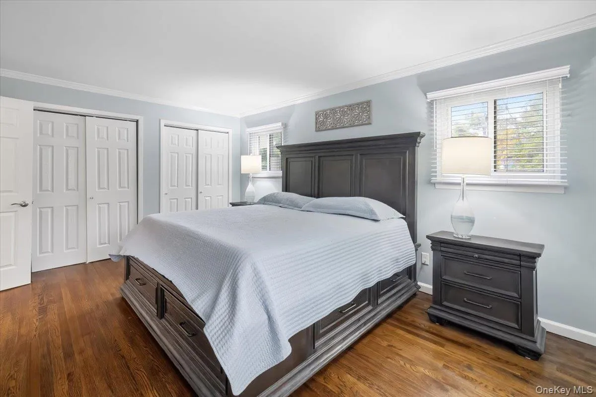 Bedroom featuring two closets, dark wood-style floors, and crown molding Bedroom featuring two closets, dark wood-style floors, and crown molding