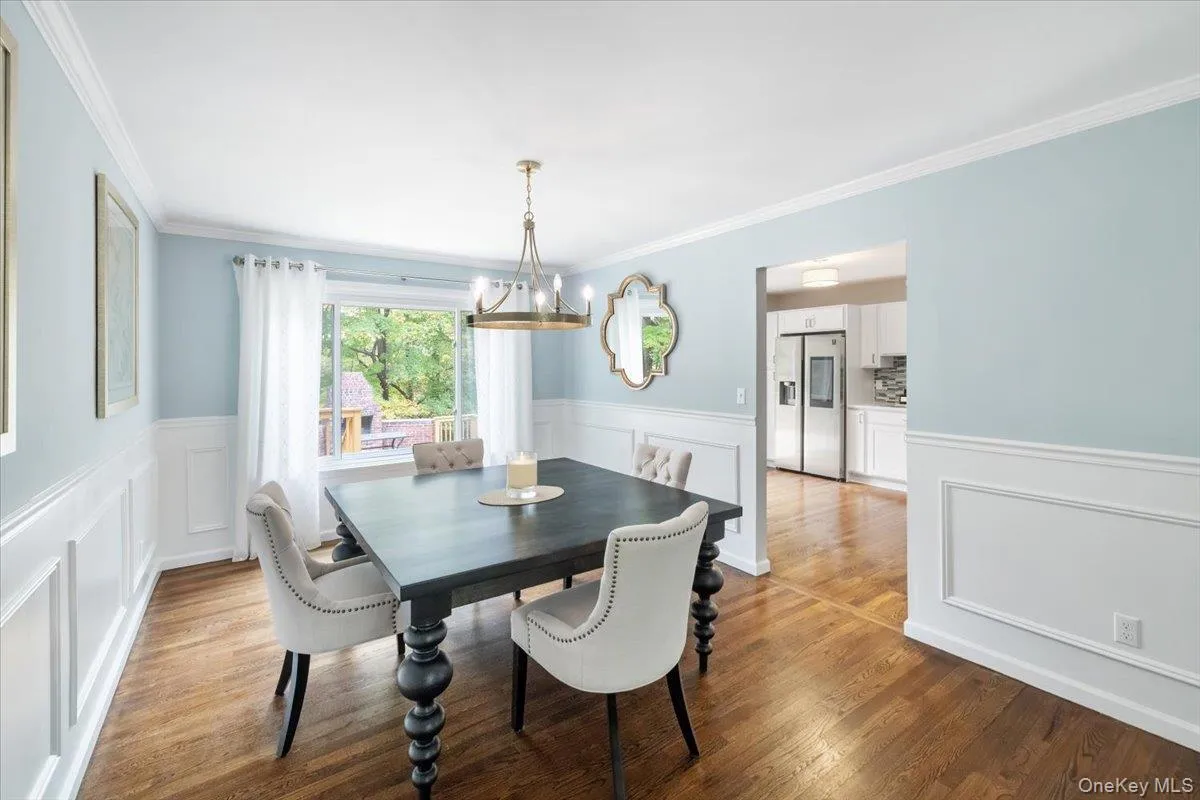 Dining room featuring a chandelier, a wainscoted wall, light wood-type flooring, crown molding, and a decorative wall Dining room featuring a chandelier, a wainscoted wall, light wood-type flooring, crown molding, and a decorative wall