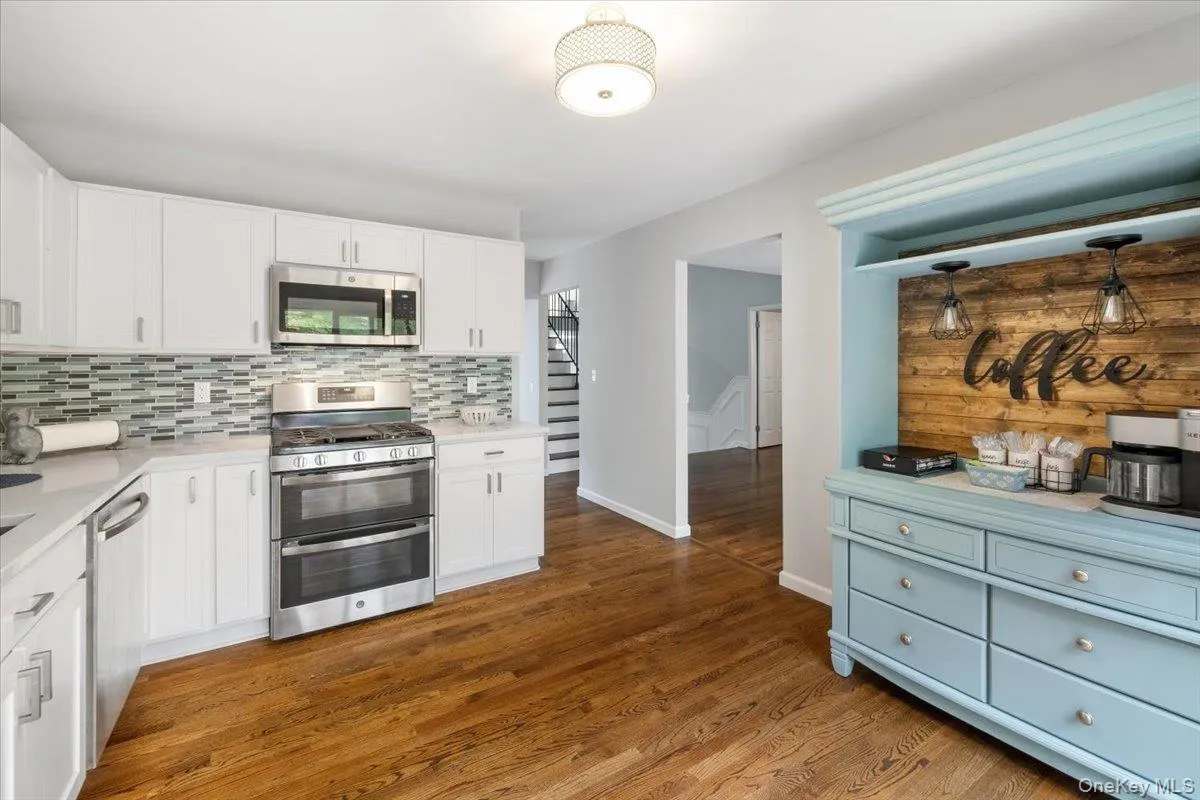 Kitchen featuring appliances with stainless steel finishes, white cabinets, dark wood-style flooring, and light stone counters Kitchen featuring appliances with stainless steel finishes, white cabinets, dark wood-style flooring, and light stone counters
