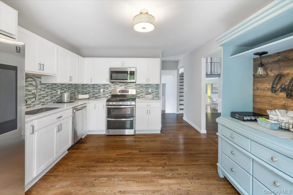 Kitchen featuring appliances with stainless steel finishes, white cabinetry, dark wood-style floors, light stone counters, and decorative backsplash Kitchen featuring appliances with stainless steel finishes, white cabinetry, dark wood-style floors, light stone counters, and decorative backsplash