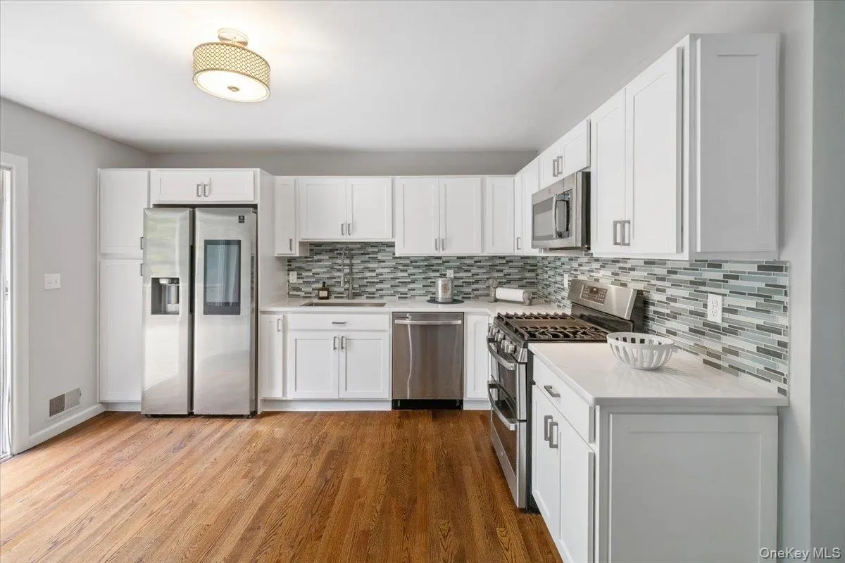 Kitchen with stainless steel appliances, white cabinetry, light wood-style floors, backsplash, and light stone countertops Kitchen with stainless steel appliances, white cabinetry, light wood-style floors, backsplash, and light stone countertops