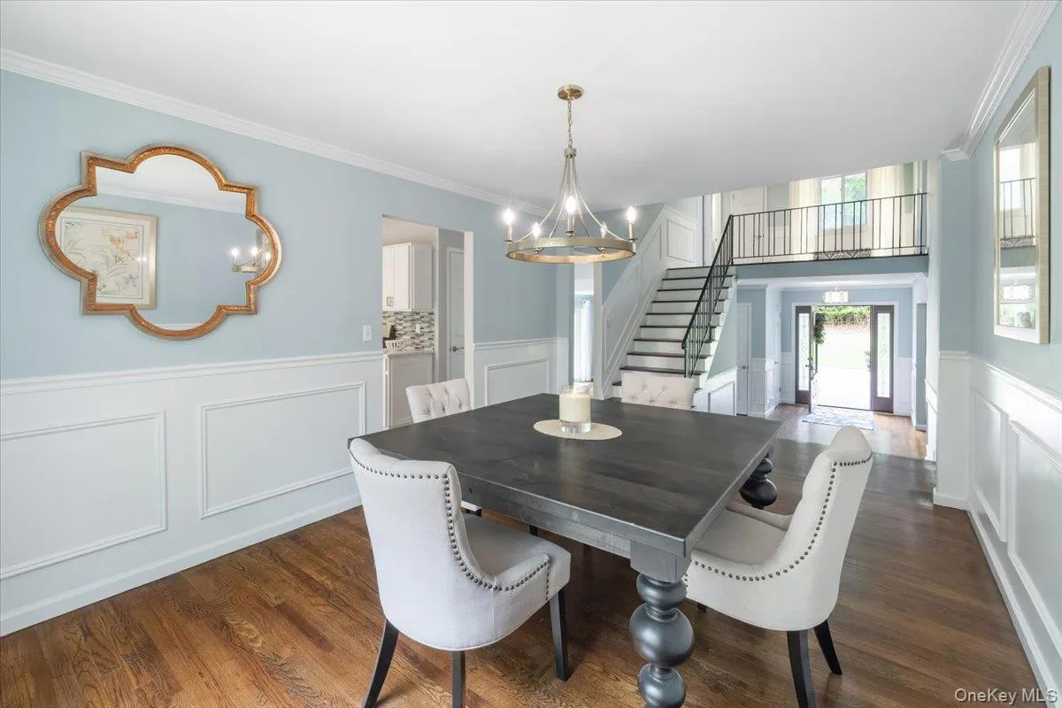 Dining area with stairs, wainscoting, a decorative wall, crown molding, and dark wood-style floors Dining area with stairs, wainscoting, a decorative wall, crown molding, and dark wood-style floors
