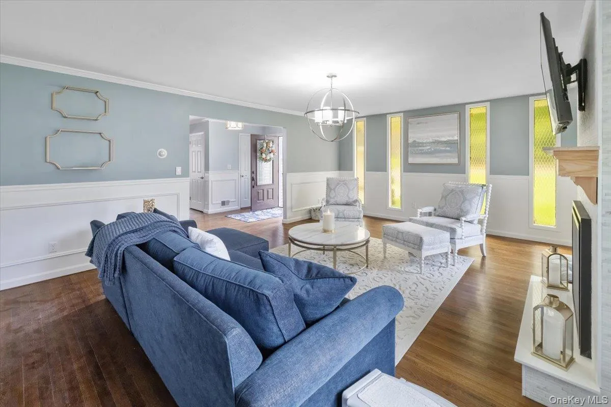 Living room with dark wood-style flooring, a fireplace, wainscoting, and a chandelier Living room with dark wood-style flooring, a fireplace, wainscoting, and a chandelier