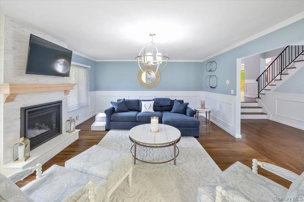 Living area with dark wood-style flooring, a large fireplace, stairs, a chandelier, and ornamental molding Living area with dark wood-style flooring, a large fireplace, stairs, a chandelier, and ornamental molding