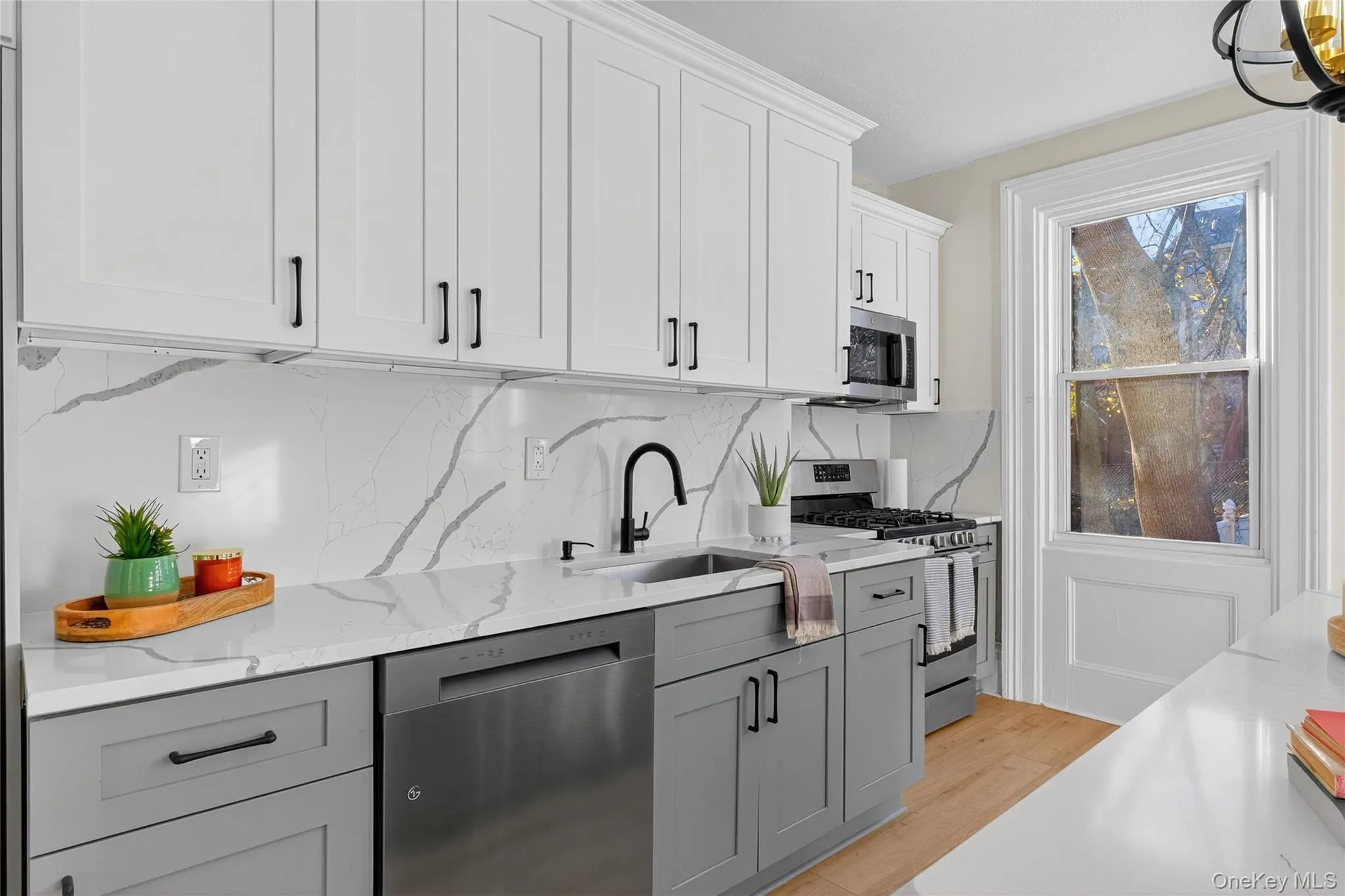 Kitchen with gray cabinets, white cabinets, appliances with stainless steel finishes, light stone counters, and tasteful backsplash Kitchen with gray cabinets, white cabinets, appliances with stainless steel finishes, light stone counters, and tasteful backsplash