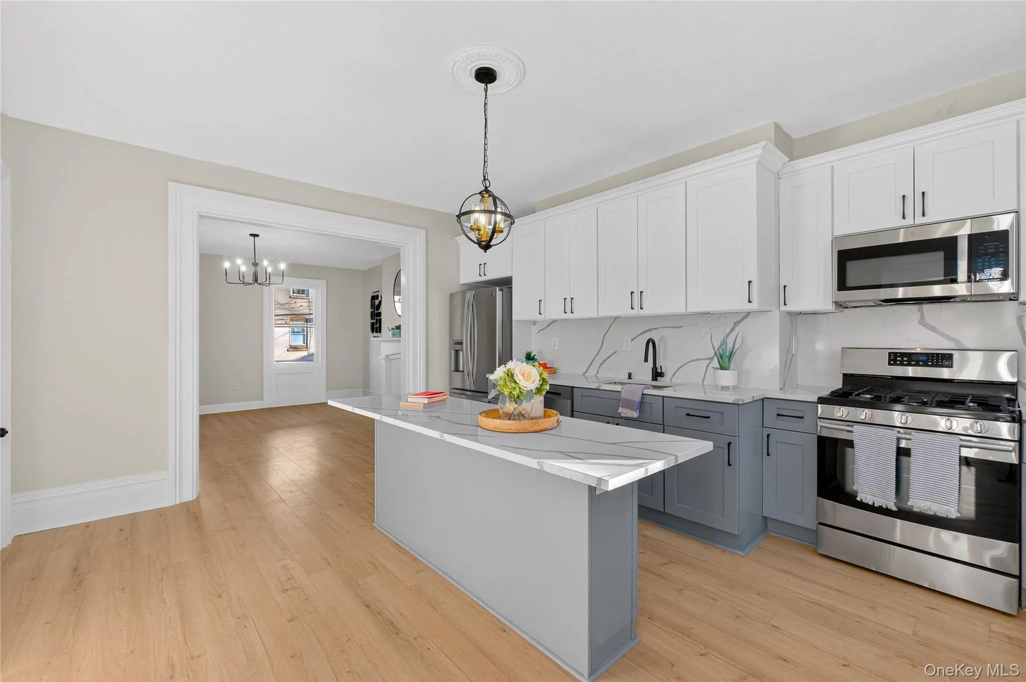 Kitchen with gray cabinets, appliances with stainless steel finishes, white cabinetry, pendant lighting, and light wood finished floors Kitchen with gray cabinets, appliances with stainless steel finishes, white cabinetry, pendant lighting, and light wood finished floors