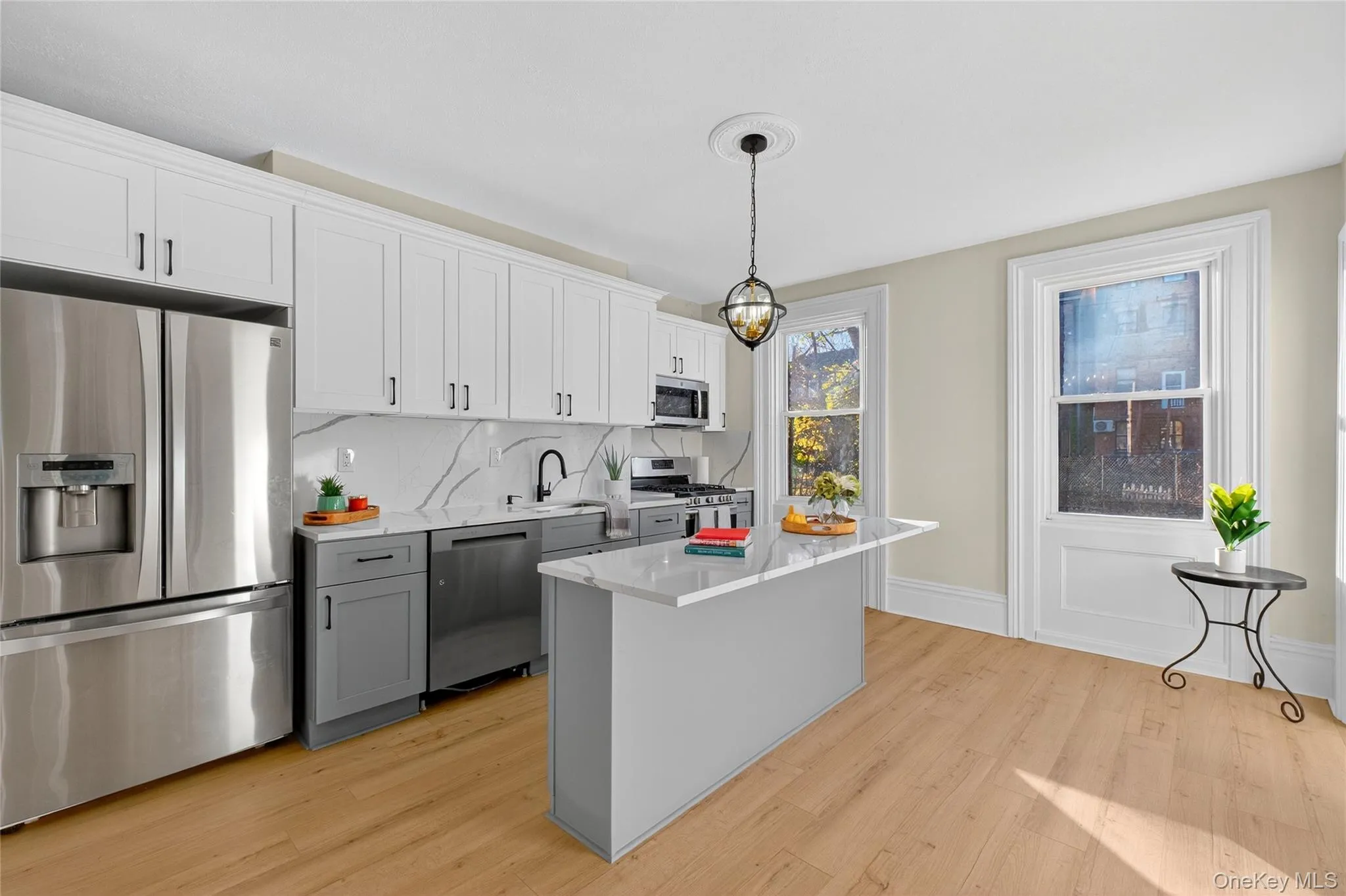 Kitchen with stainless steel appliances, gray cabinets, white cabinets, light wood-type flooring, and decorative light fixtures Kitchen with stainless steel appliances, gray cabinets, white cabinets, light wood-type flooring, and decorative light fixtures