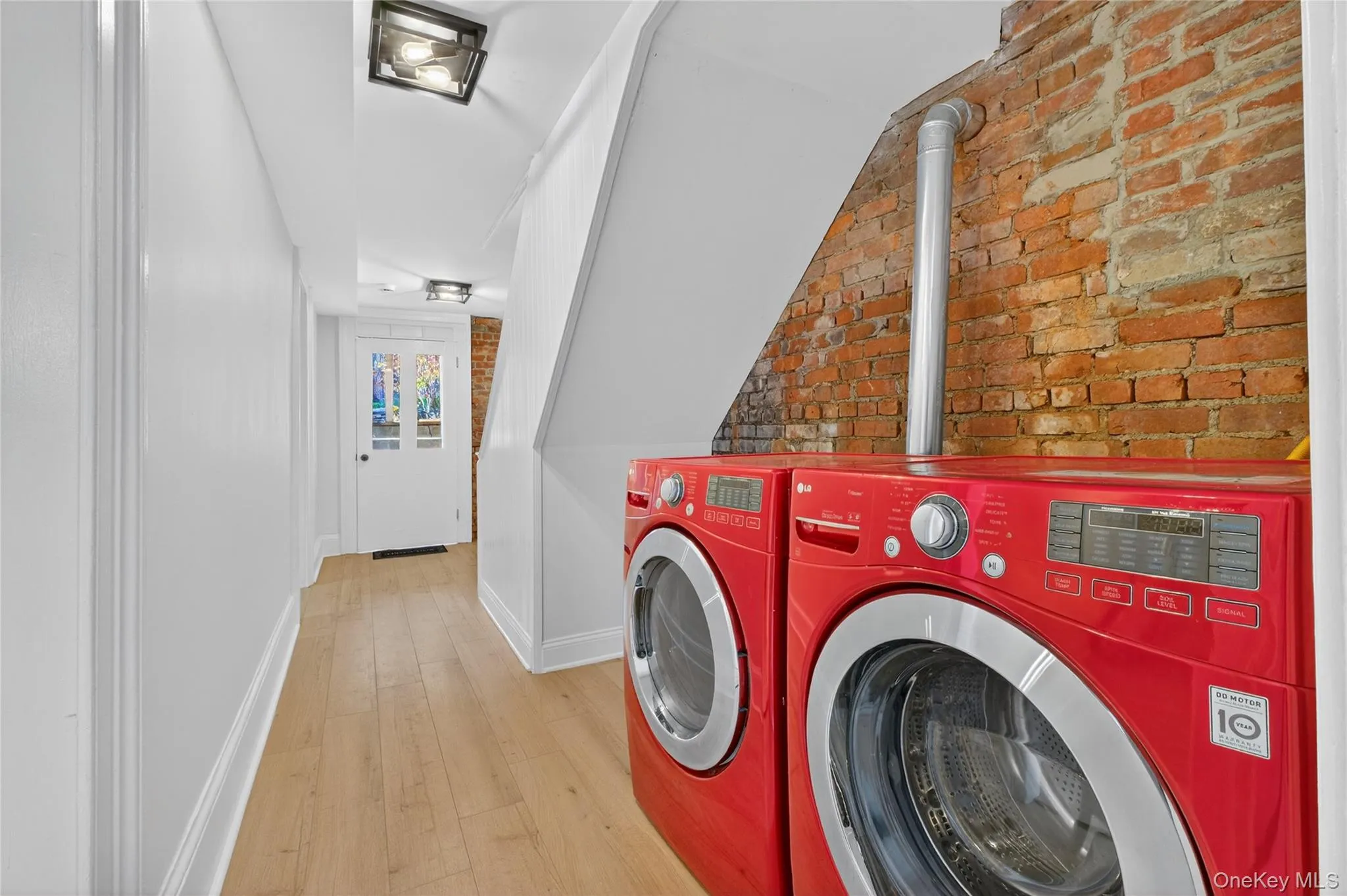 Laundry room with brick wall, light wood-style floors, and washer and clothes dryer Laundry room with brick wall, light wood-style floors, and washer and clothes dryer