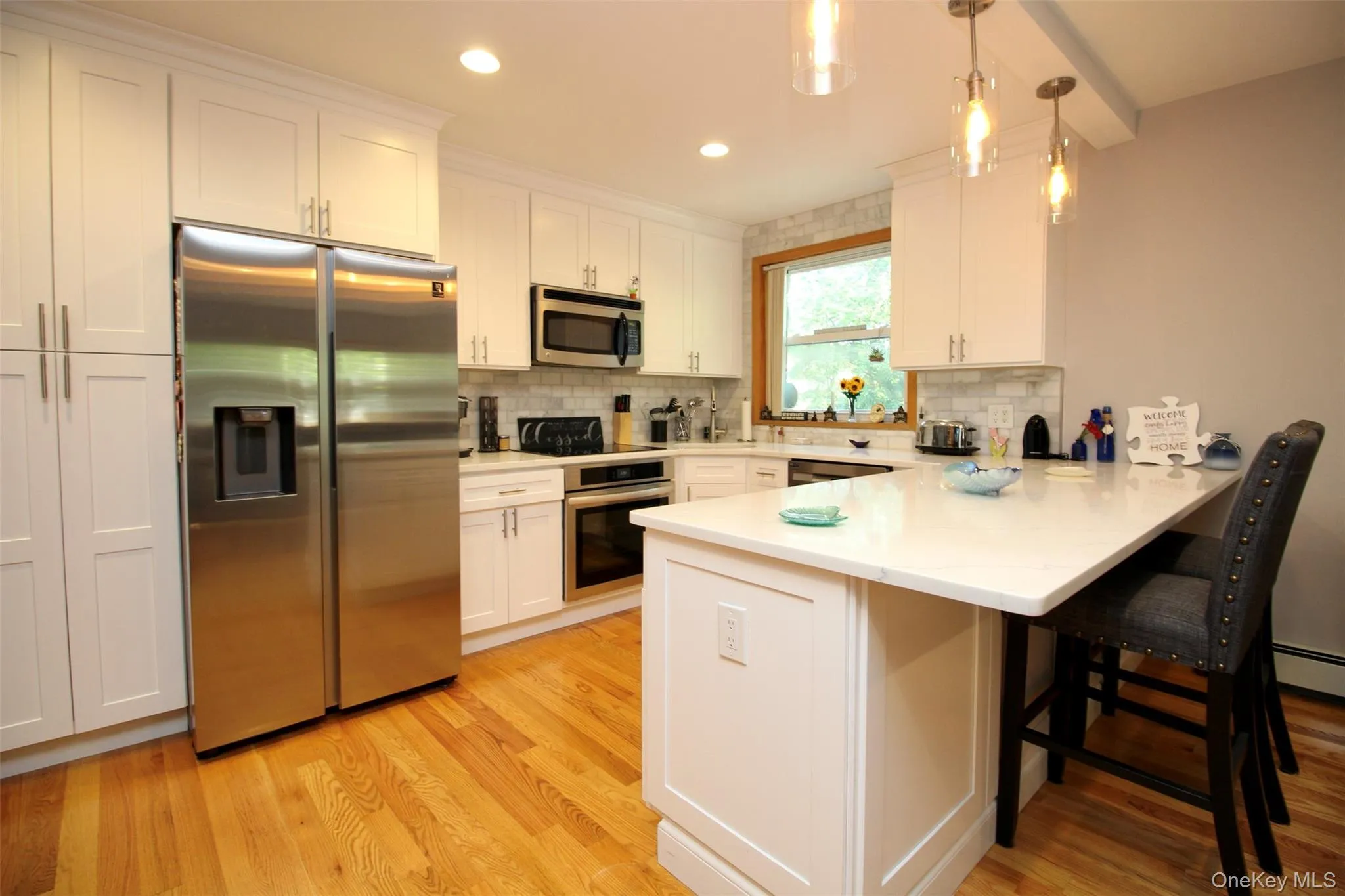Kitchen with appliances with stainless steel finishes, a peninsula, tasteful backsplash, light wood-type flooring, and hanging light fixtures Kitchen with appliances with stainless steel finishes, a peninsula, tasteful backsplash, light wood-type flooring, and hanging light fixtures