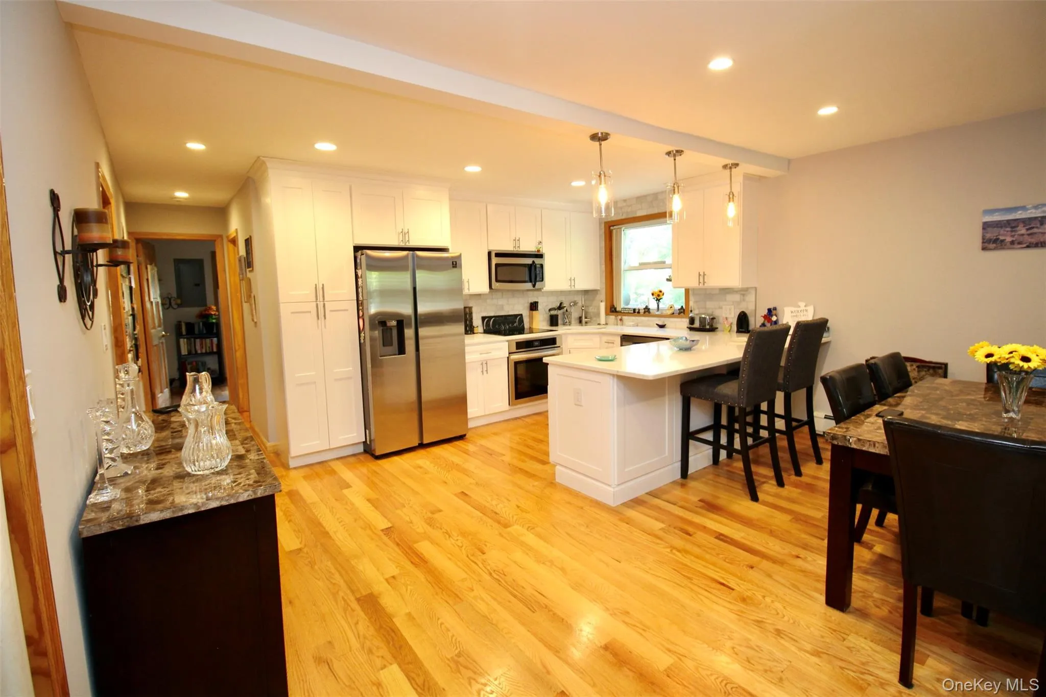 Kitchen with stainless steel appliances, white cabinetry, hanging light fixtures, light wood-type flooring, and a peninsula Kitchen with stainless steel appliances, white cabinetry, hanging light fixtures, light wood-type flooring, and a peninsula