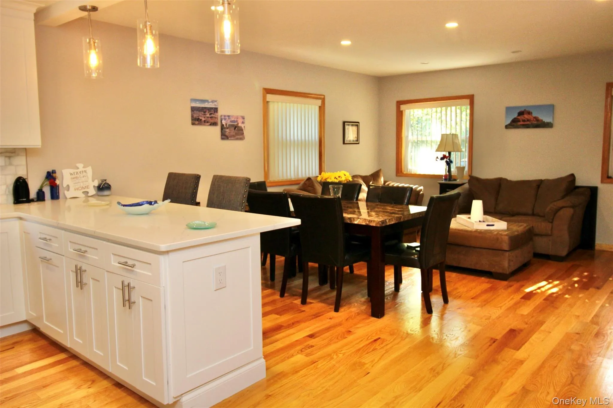 Kitchen with open floor plan, a peninsula, white cabinetry, hanging light fixtures, and light wood finished floors Kitchen with open floor plan, a peninsula, white cabinetry, hanging light fixtures, and light wood finished floors