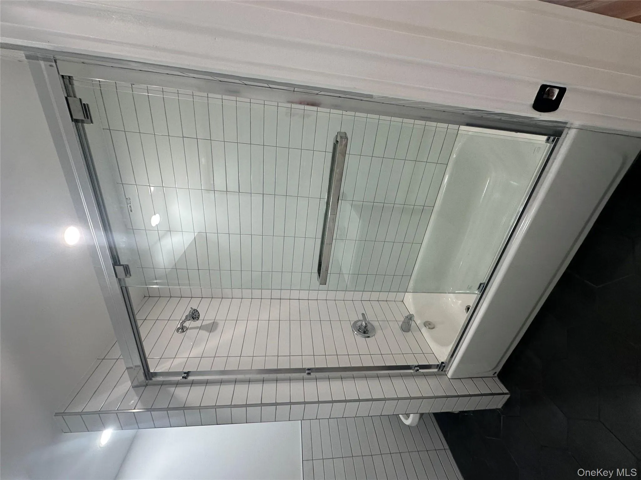 Bathroom with combined bath / shower with glass door, tile walls, and dark tile patterned flooring Bathroom with combined bath / shower with glass door, tile walls, and dark tile patterned flooring