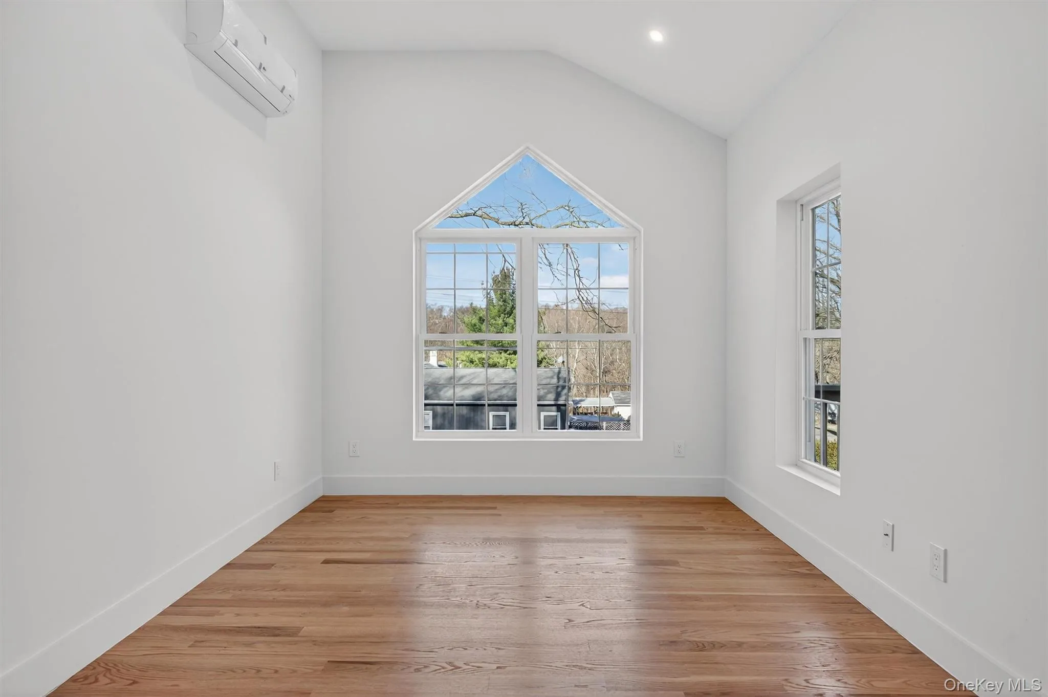Spare room with light wood finished floors, vaulted ceiling, a wall mounted AC, and recessed lighting Spare room with light wood finished floors, vaulted ceiling, a wall mounted AC, and recessed lighting