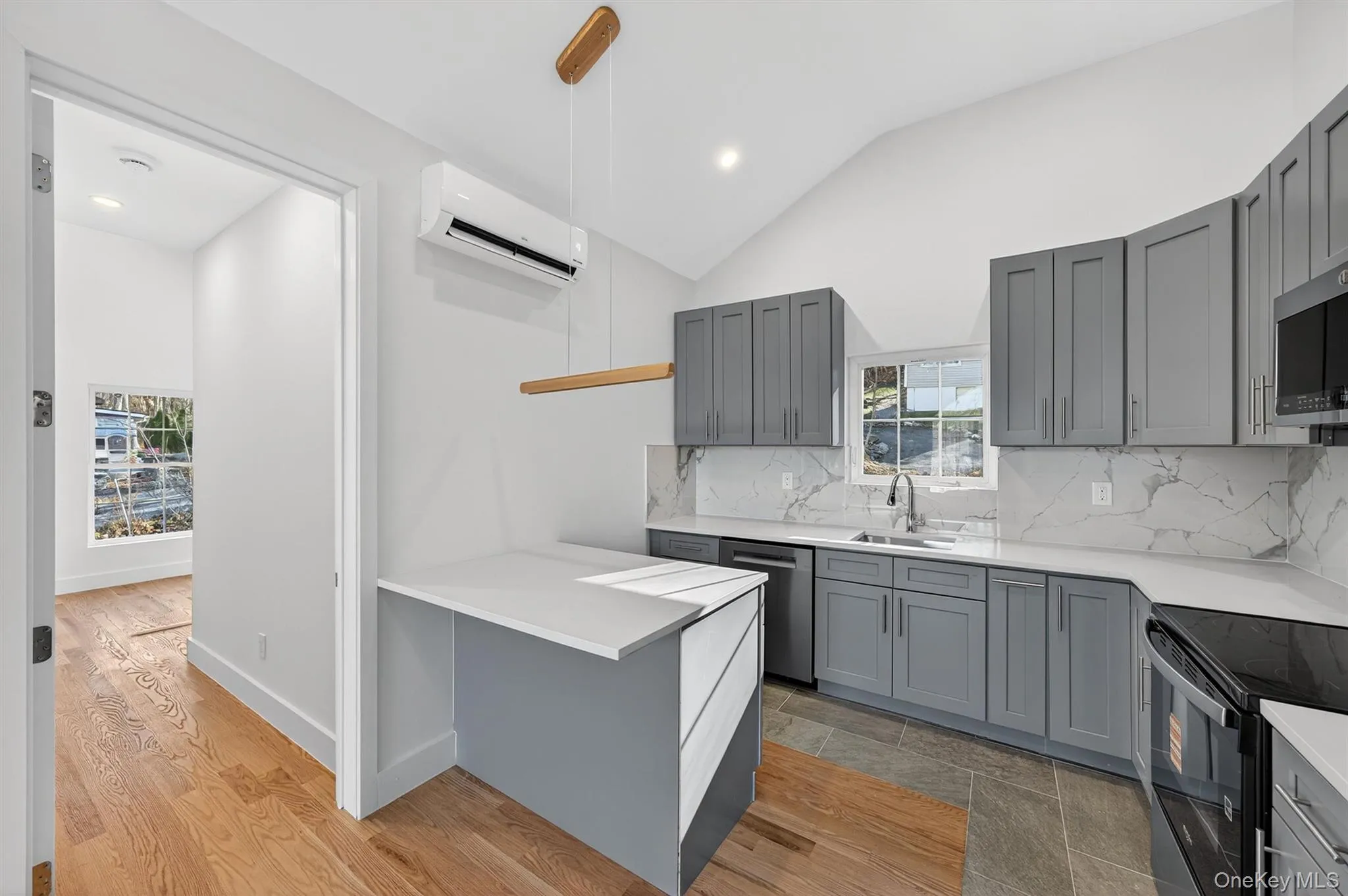 Kitchen featuring gray cabinets, vaulted ceiling, appliances with stainless steel finishes, backsplash, and hanging light fixtures Kitchen featuring gray cabinets, vaulted ceiling, appliances with stainless steel finishes, backsplash, and hanging light fixtures