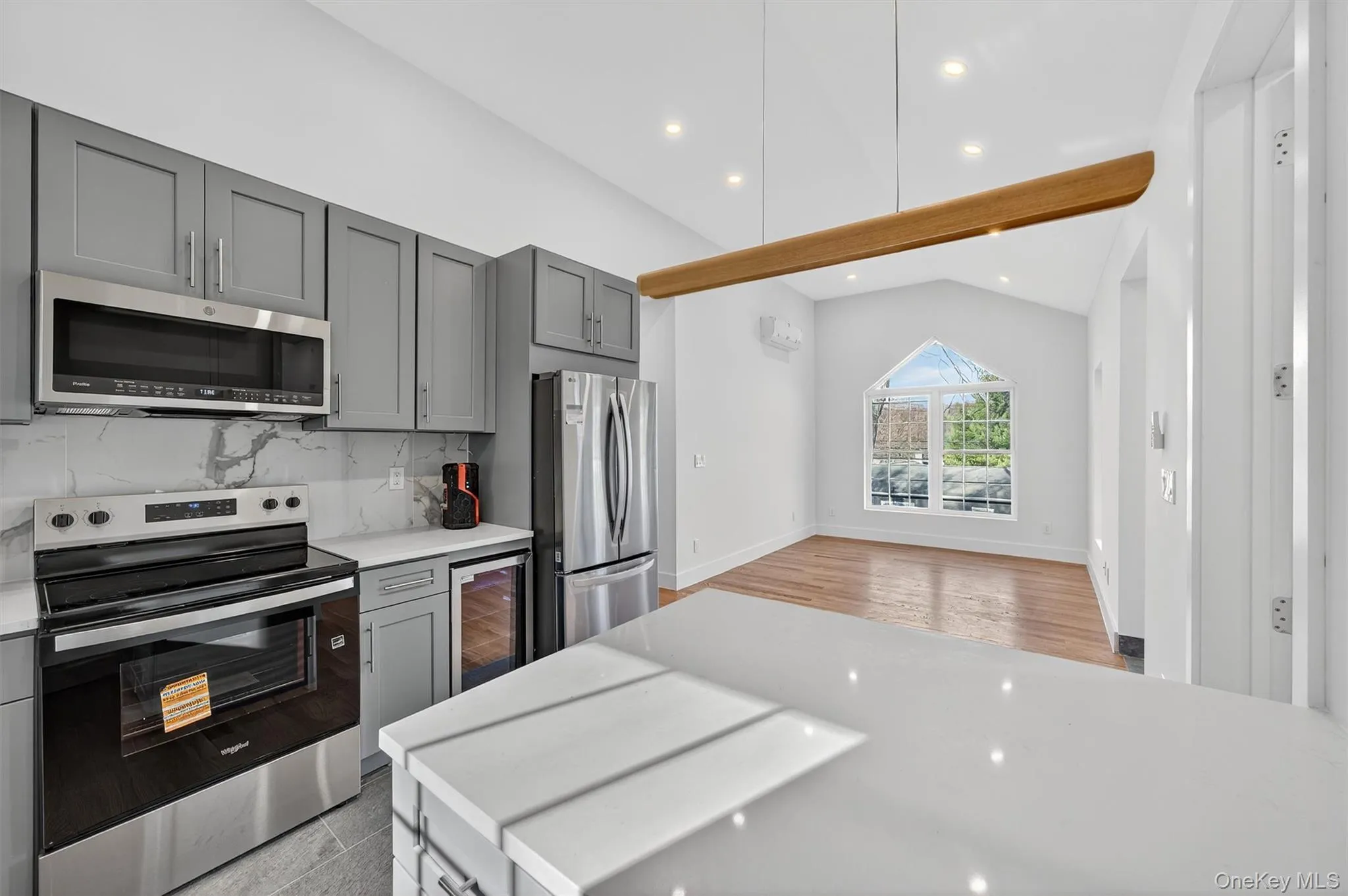 Kitchen featuring appliances with stainless steel finishes, gray cabinetry, tasteful backsplash, lofted ceiling, and wine cooler Kitchen featuring appliances with stainless steel finishes, gray cabinetry, tasteful backsplash, lofted ceiling, and wine cooler