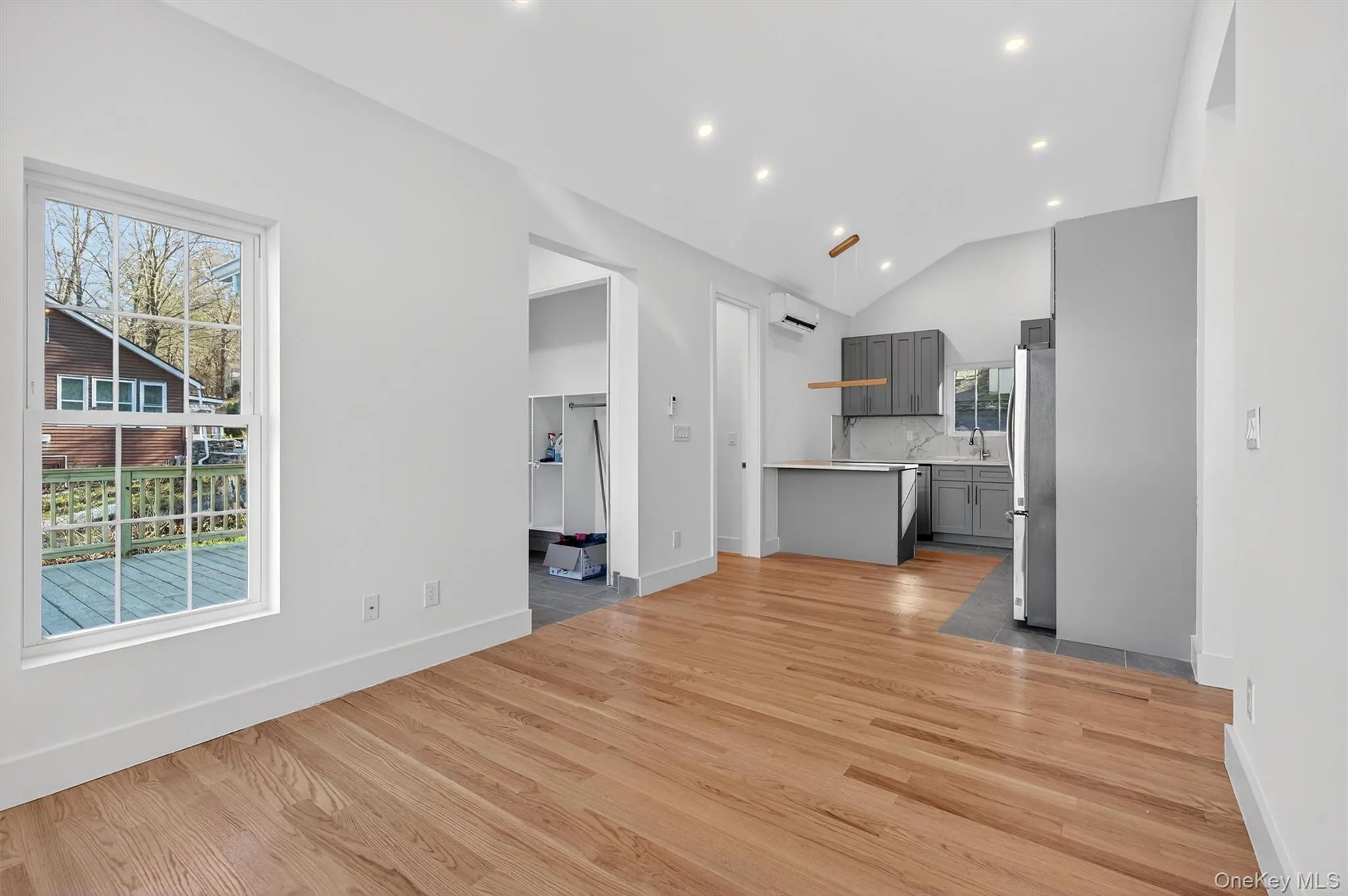 Unfurnished living room with light wood-style flooring, lofted ceiling, recessed lighting, and a wall unit AC Unfurnished living room with light wood-style flooring, lofted ceiling, recessed lighting, and a wall unit AC