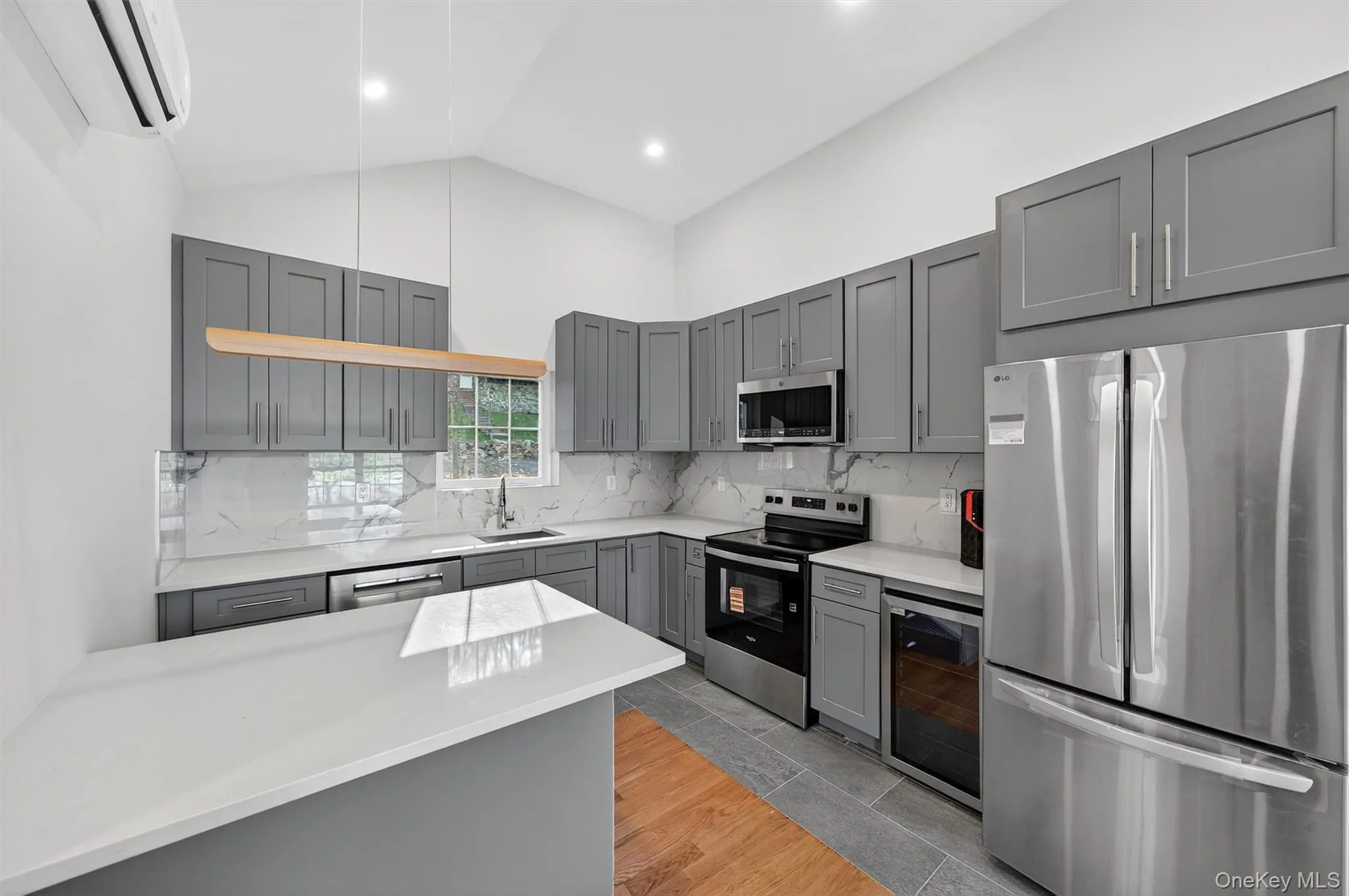 Kitchen with stainless steel appliances, gray cabinetry, wine cooler, backsplash, and high vaulted ceiling Kitchen with stainless steel appliances, gray cabinetry, wine cooler, backsplash, and high vaulted ceiling
